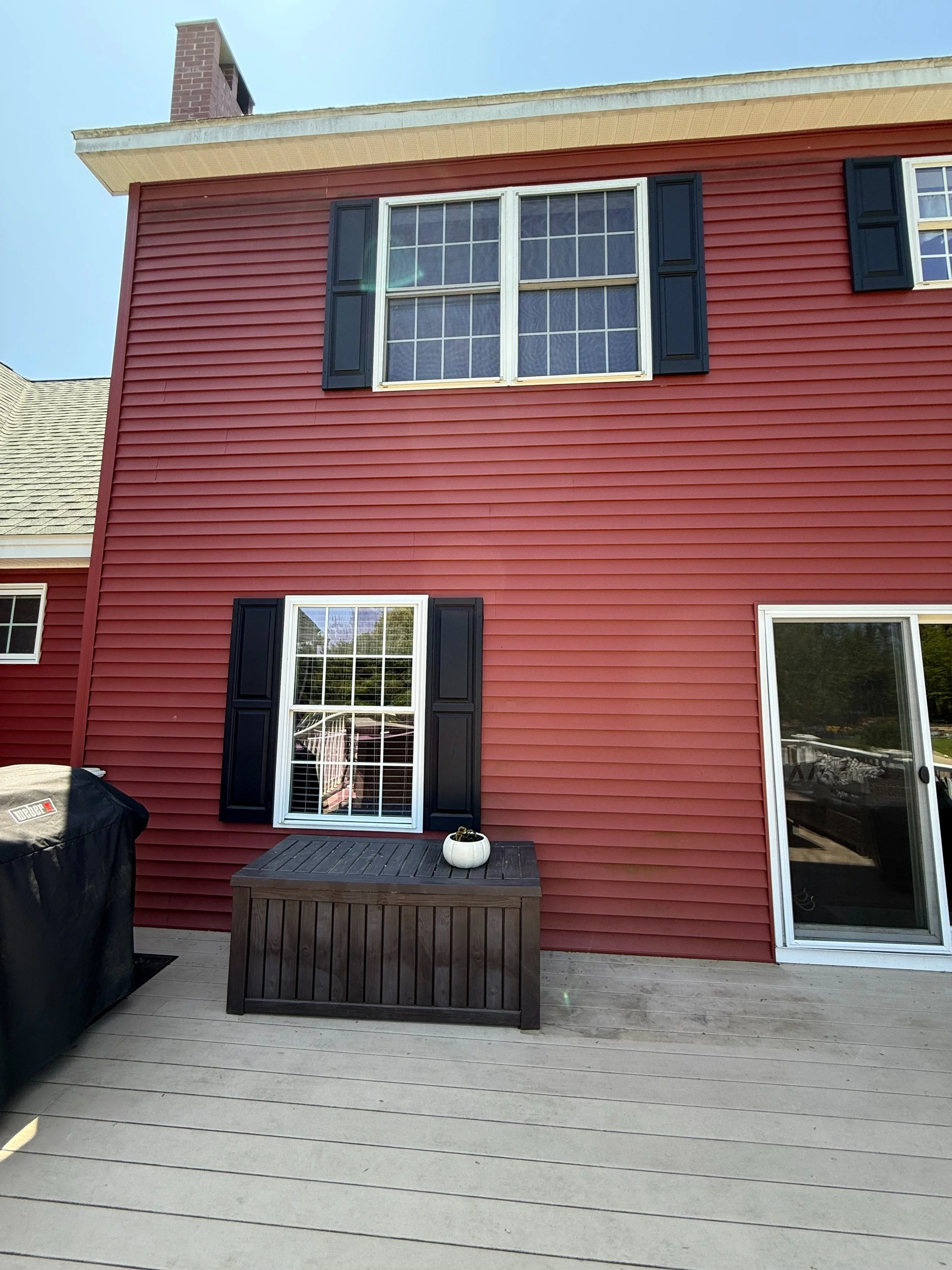 Red house with black shutters, large window, sliding door, and outdoor deck with a small pumpkin decoration.