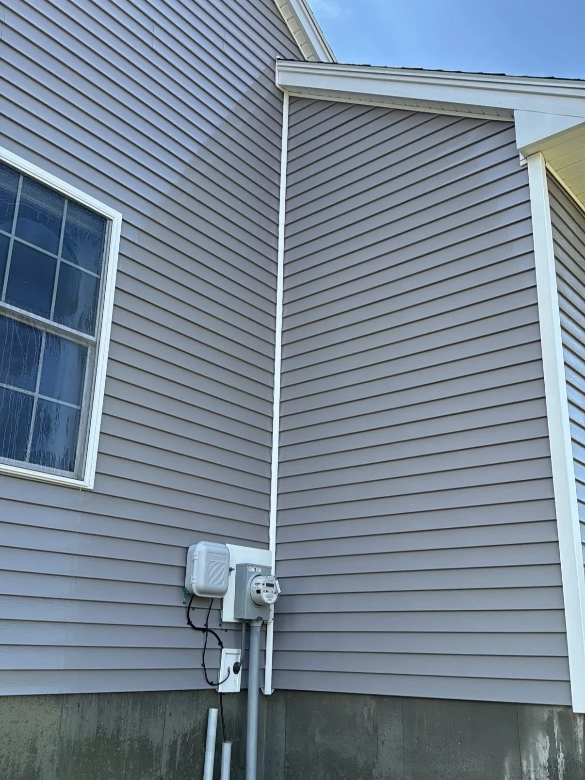 Exterior view of a house corner with vinyl siding, window, and electrical meters.