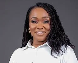 Portrait of a woman with long, curly hair wearing a white blouse against a gray background.