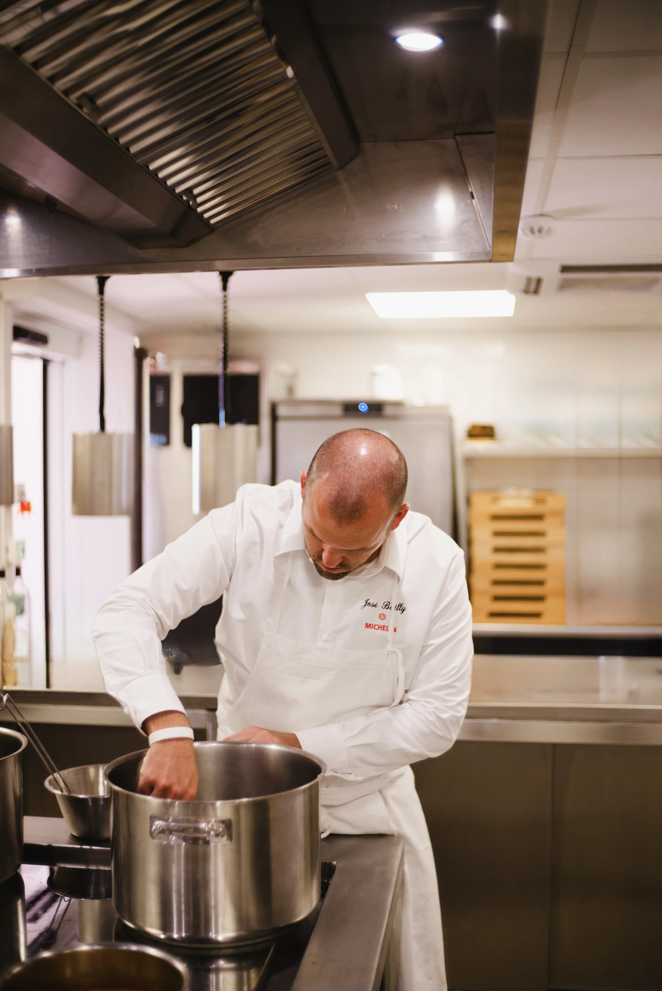 A chef in a white uniform working in a commercial kitchen with stainless steel appliances.