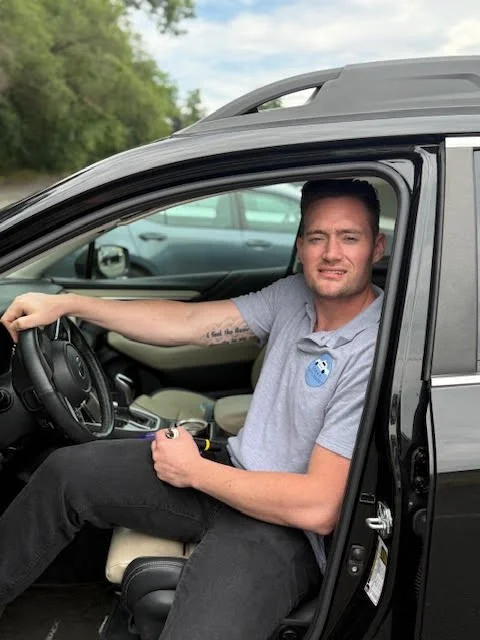 A young man holding a small French Bulldog puppy indoors, smiling at the camera.