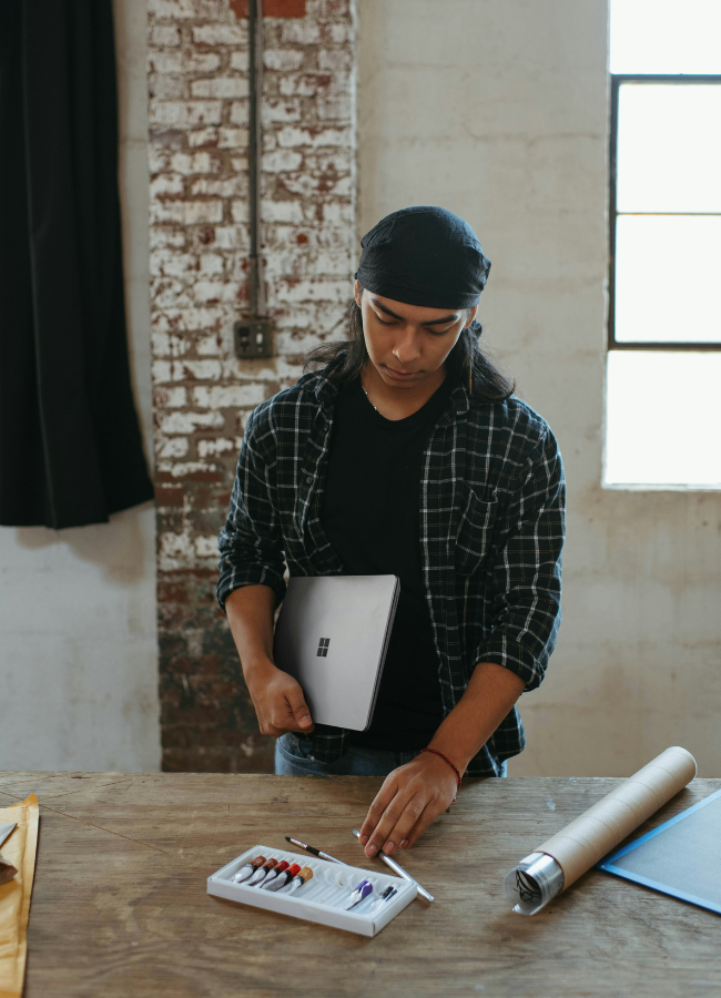 Photo of man holding a laptop, picking up his painting supplies