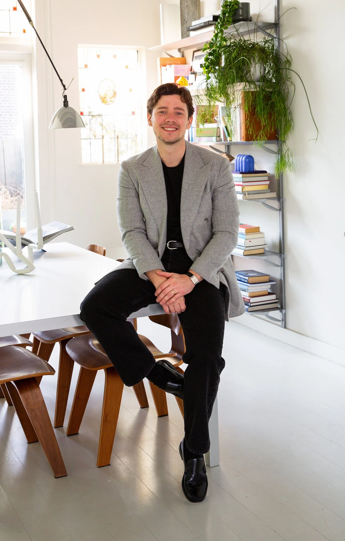 Man sitting on a table in a modern home office with books and plants on shelves.