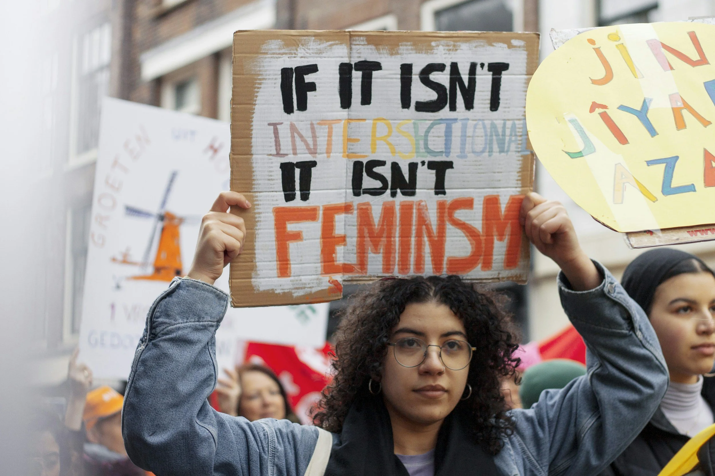 femme person holding a sign that says "if it isn't intersectional it isn't feminism" in a protest in downtown San Diego