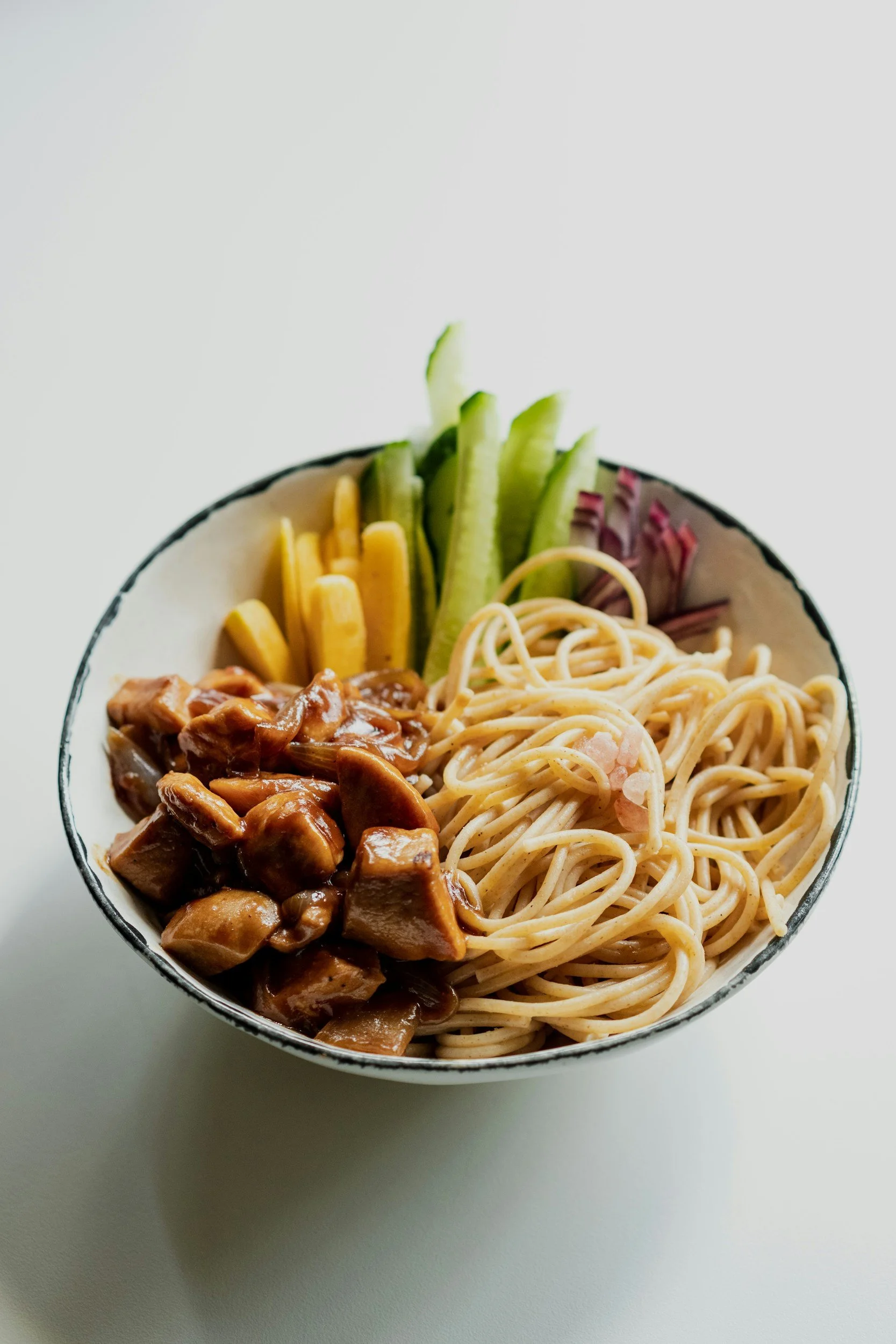 Bowl of food with noodles, colorful vegetables and meat, separated