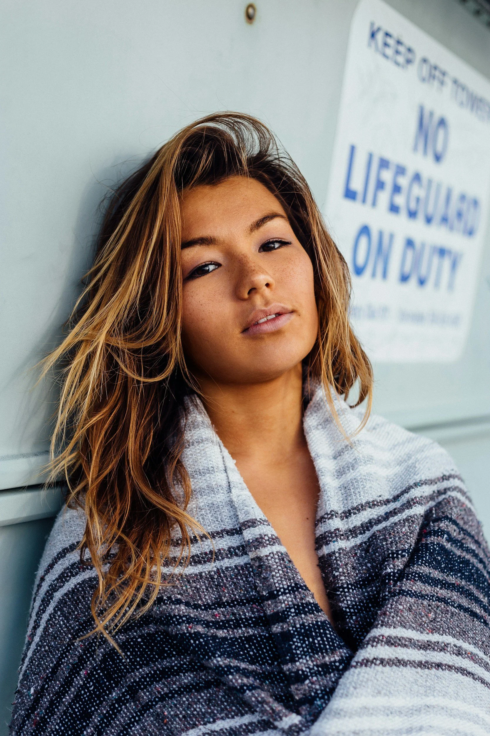 Mixed race woman standing against a white wall, wearing a blanket around her shoulders