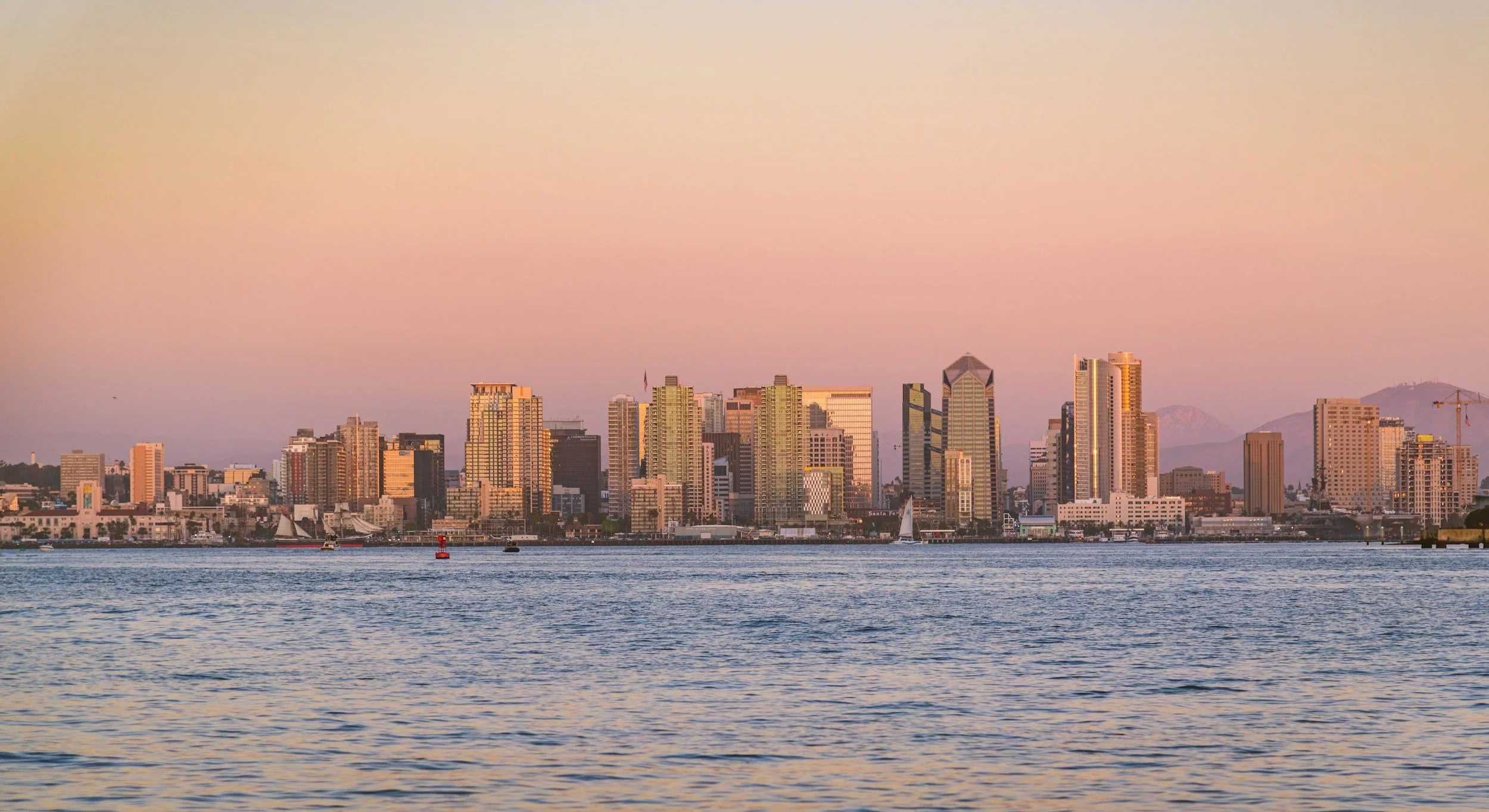 Image of San Diego city skyline with pink sunset and blue ocean water