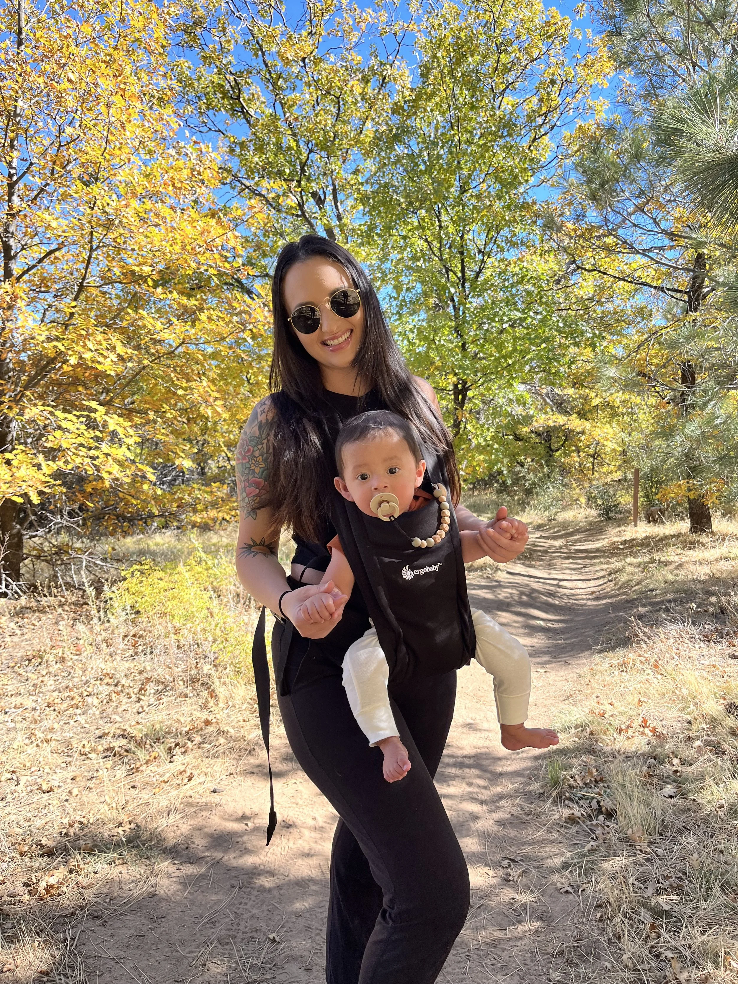 Picture of a mom holding baby in a baby carrier with  trees in the background