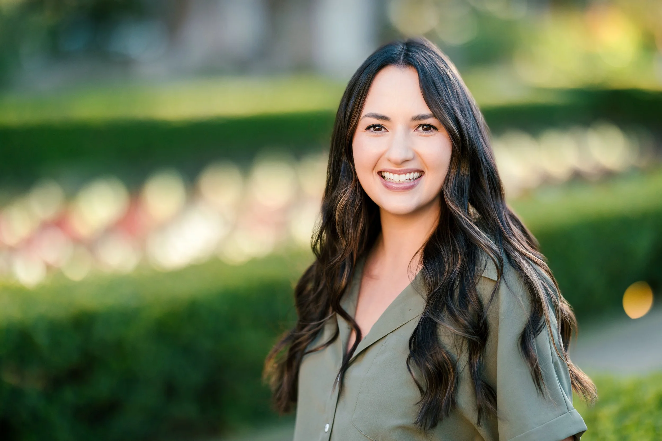 A young woman, founder of ED and OCD Therapy, with long dark hair and a light green shirt smiling outdoors in a park.