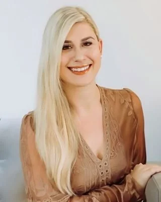 A woman with long blonde hair, smiling and wearing a brown blouse.