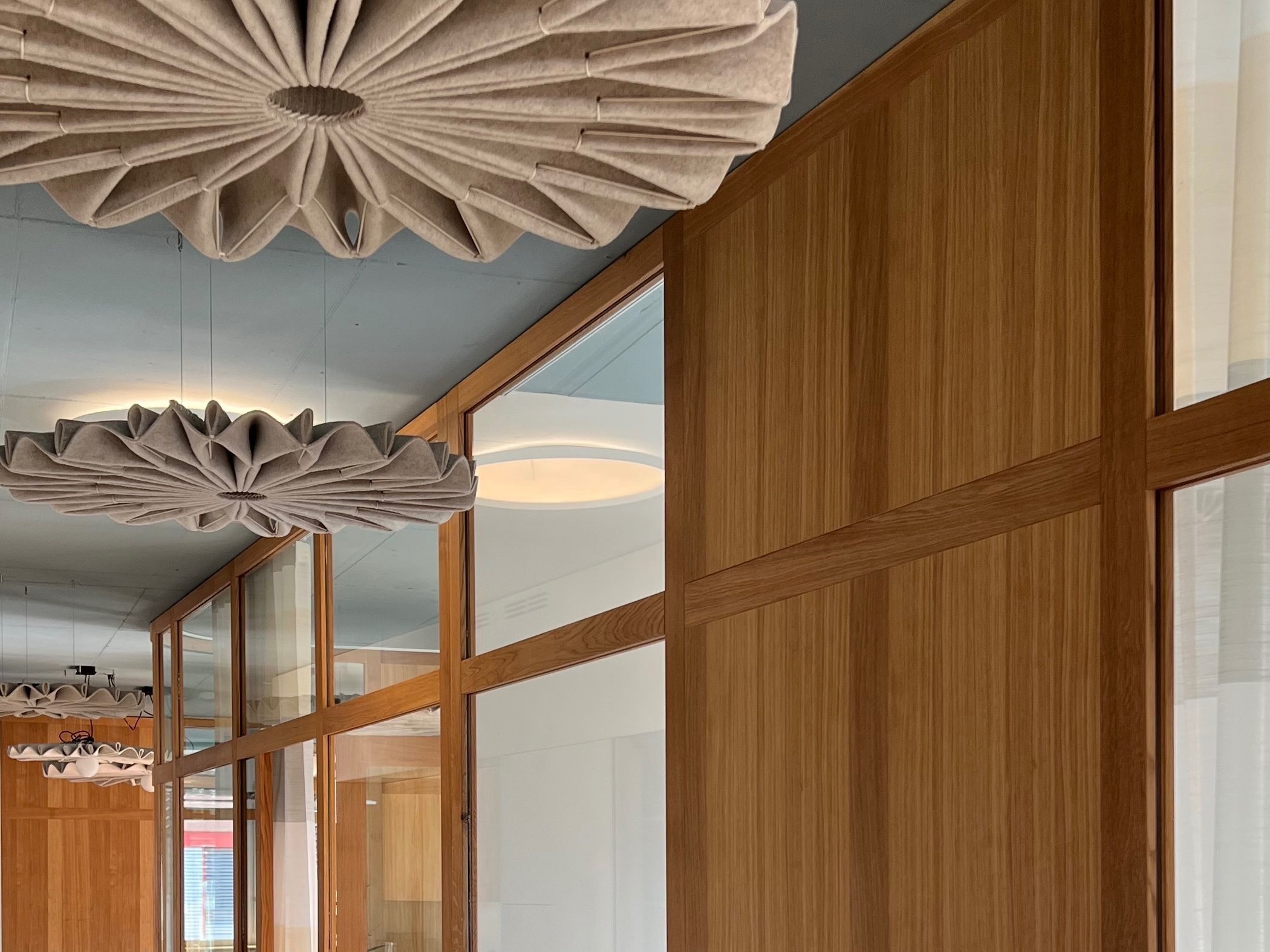 Moderne Innenarchitektur mit Holzpaneelen und dekorativen Lampen in den Büros einer Vorsorgestiftung.