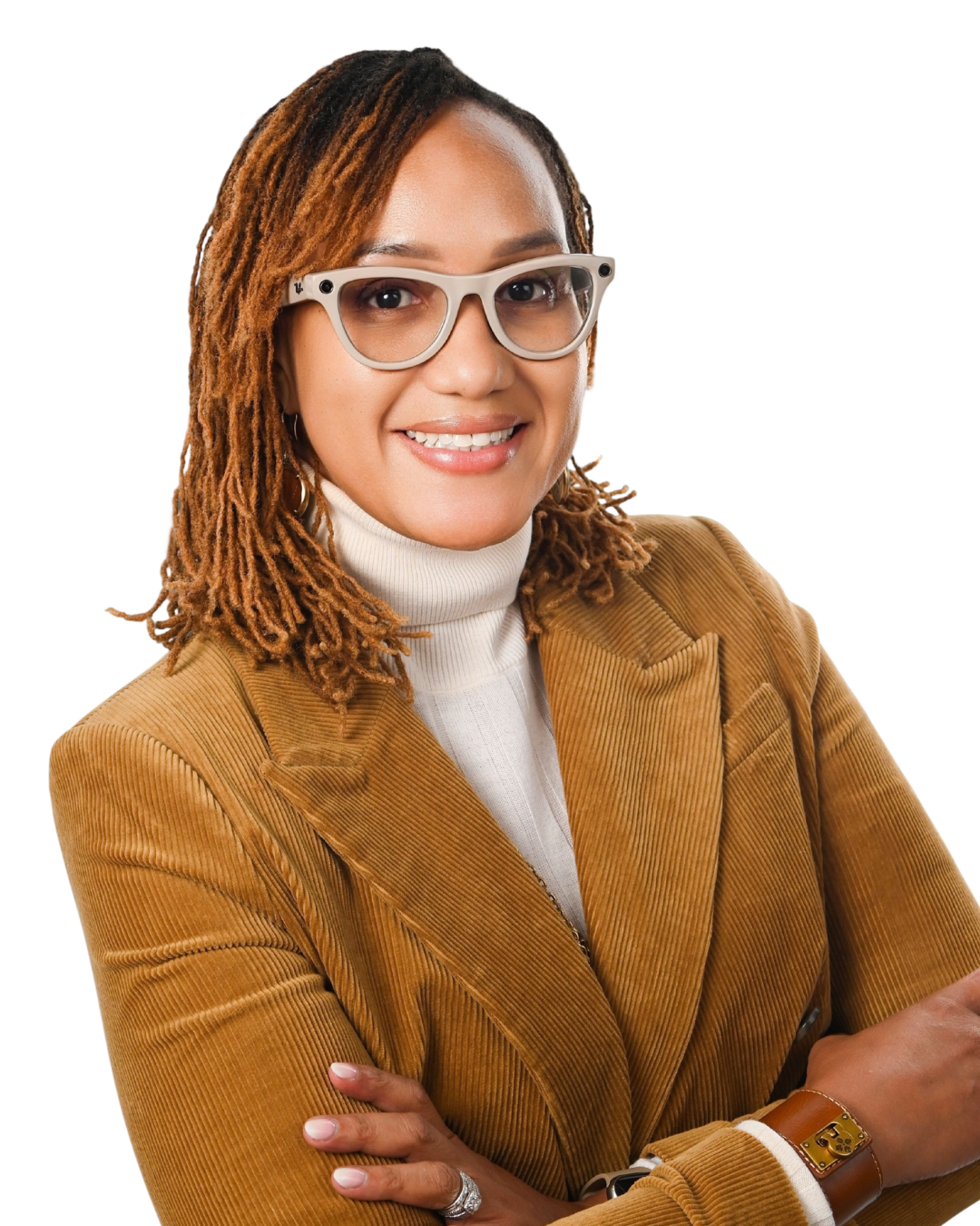A woman with short, curly, reddish-brown hair, wearing large black glasses, a yellow blazer, and a blue top, smiling with arms crossed against a white background.