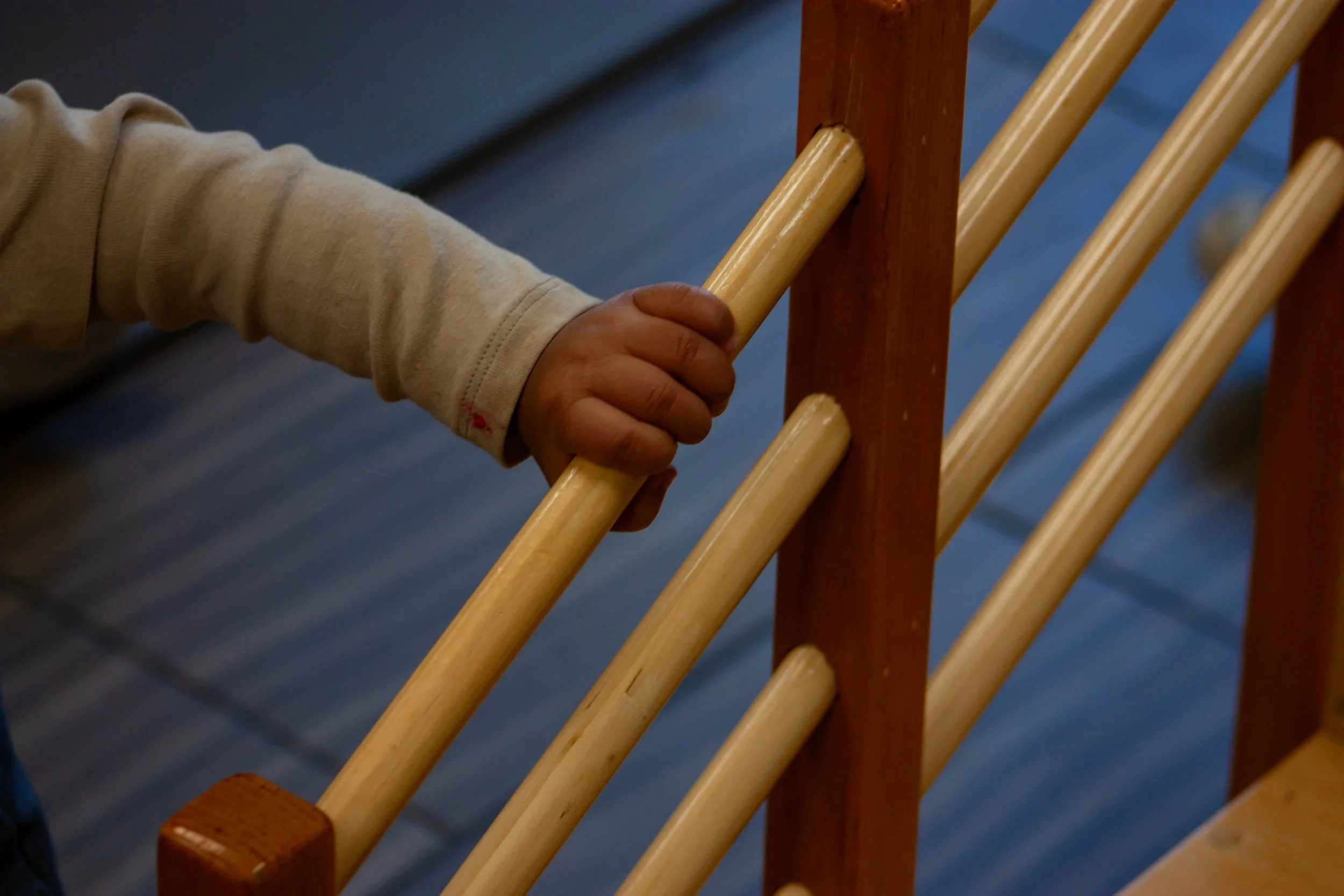 Child's hand gripping a wooden rail on a wooden staircase or railing.