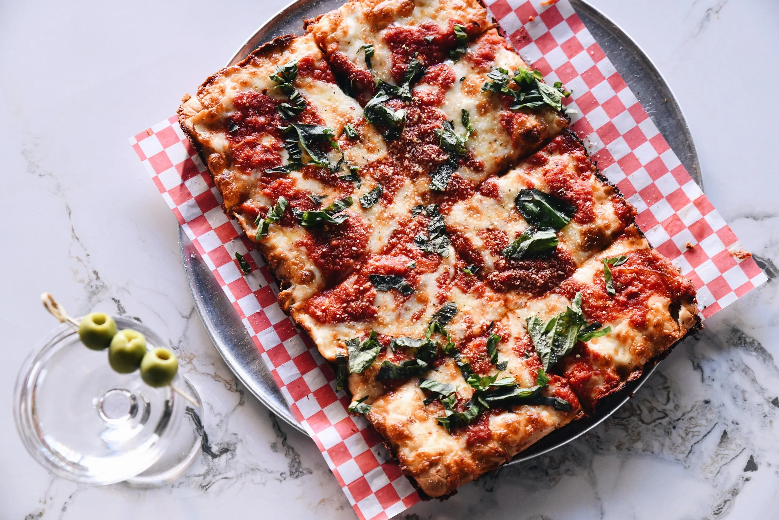 Three different Pizza Via pizzas in open cardboard boxes on checkered paper, one with pepperoni and mushrooms, another with fresh basil and tomatoes, and a third with spinach and cheese.