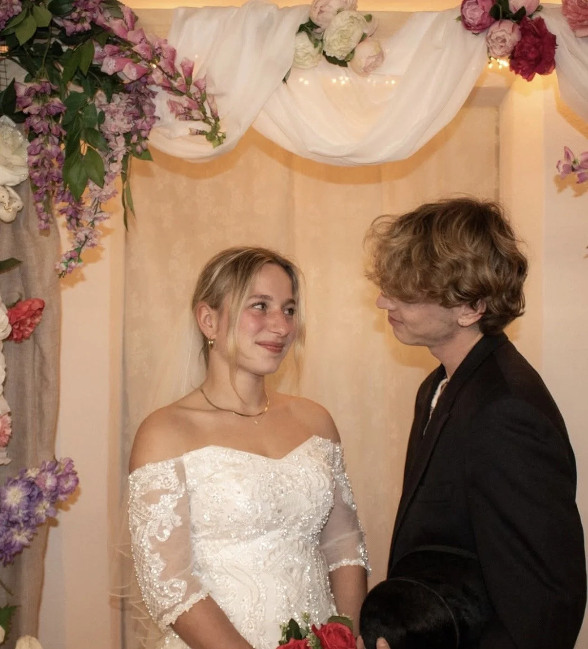 Een bruid en een bruidegom kijken elkaar liefdevol aan tijdens hun huwelijk, omringd door bloemendecoraties.