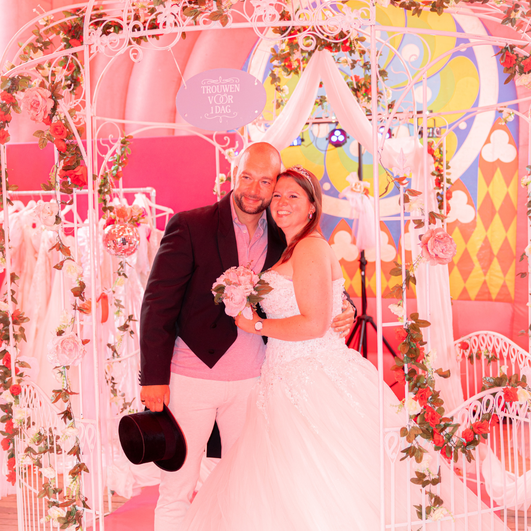 Een bruid en bruidegom poseeren op hun bruiloft in een kleurrijke, feestelijke setting met bloemen en versieringen.