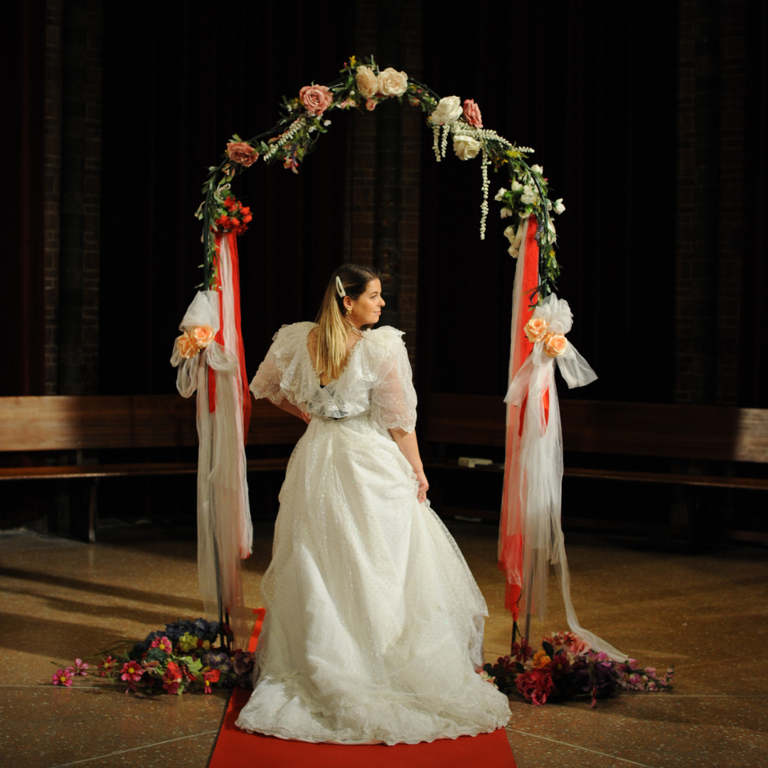 Een vrouw in een witte trouwjurk staat voor een bloemenboog tijdens een bruiloft.