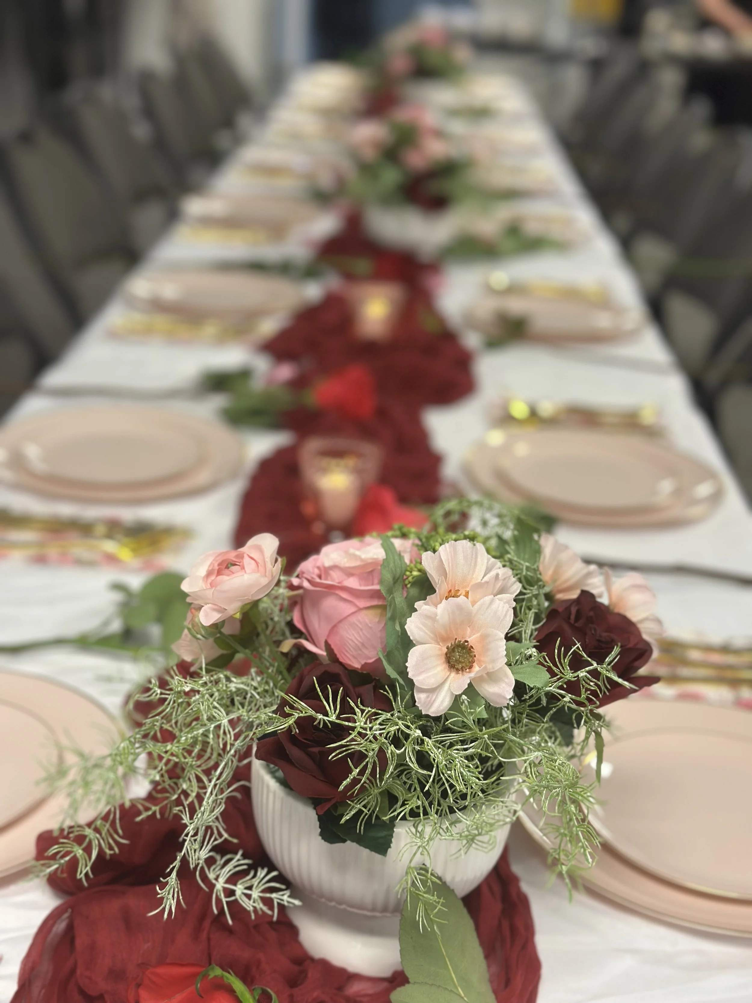floral centerpiece featuring lpink and yellow flowers on a dining table with blue plates and gold utensils