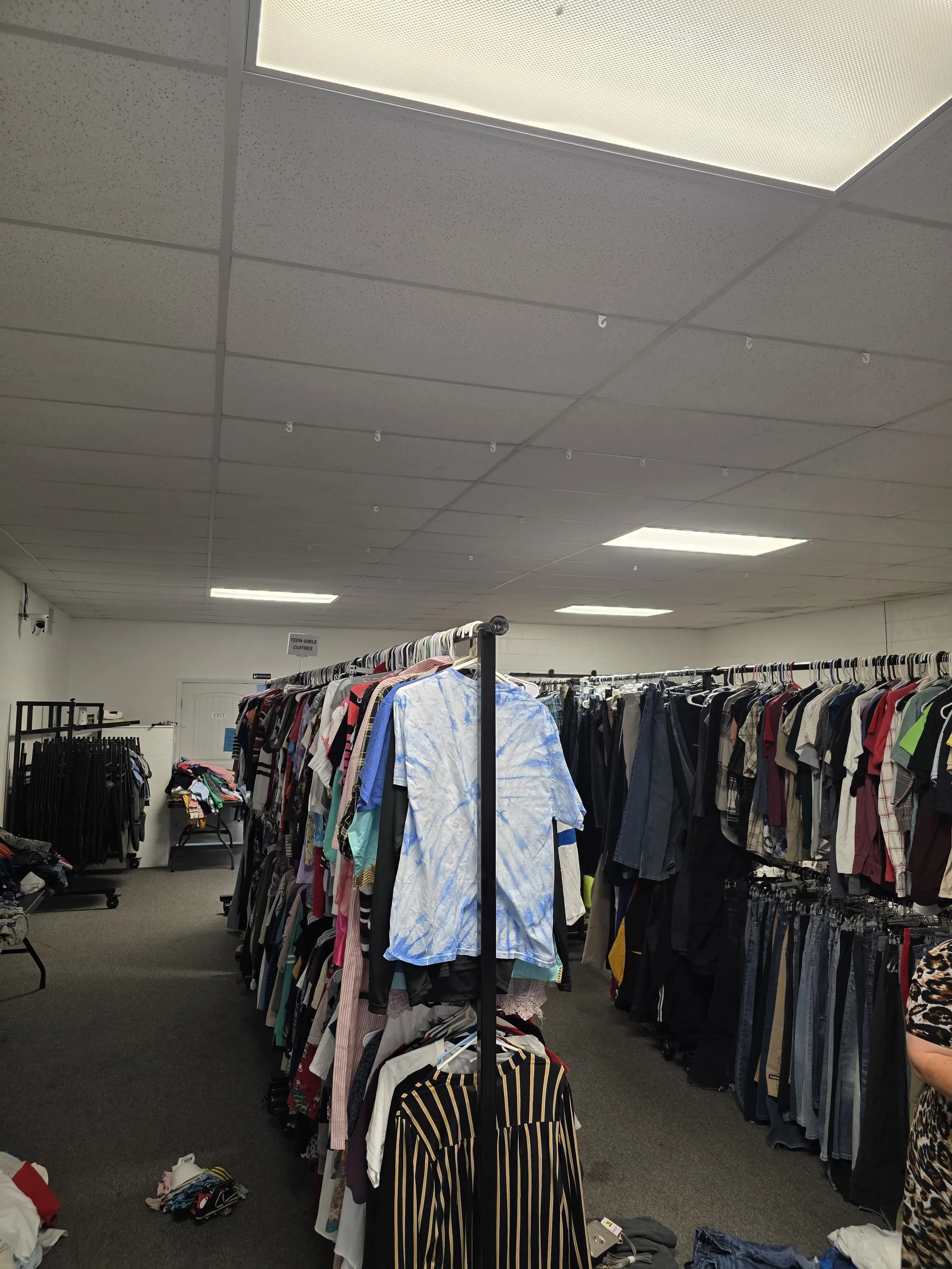 Clothing racks filled with assorted women's and men's clothes in a resale shop.