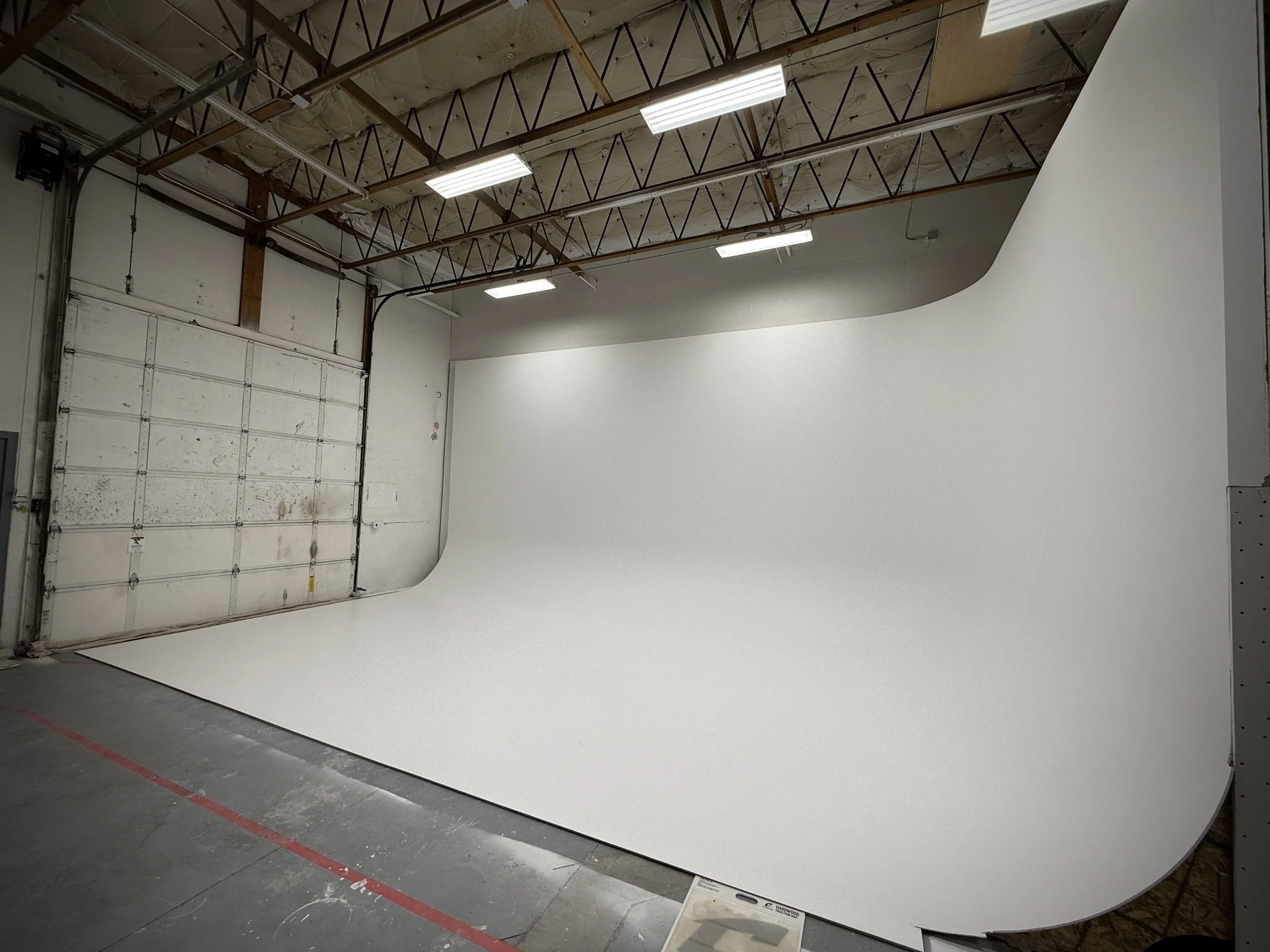Photo of an indoor photography studio with a curved white backdrop, overhead lights, and a garage door in the corner.
