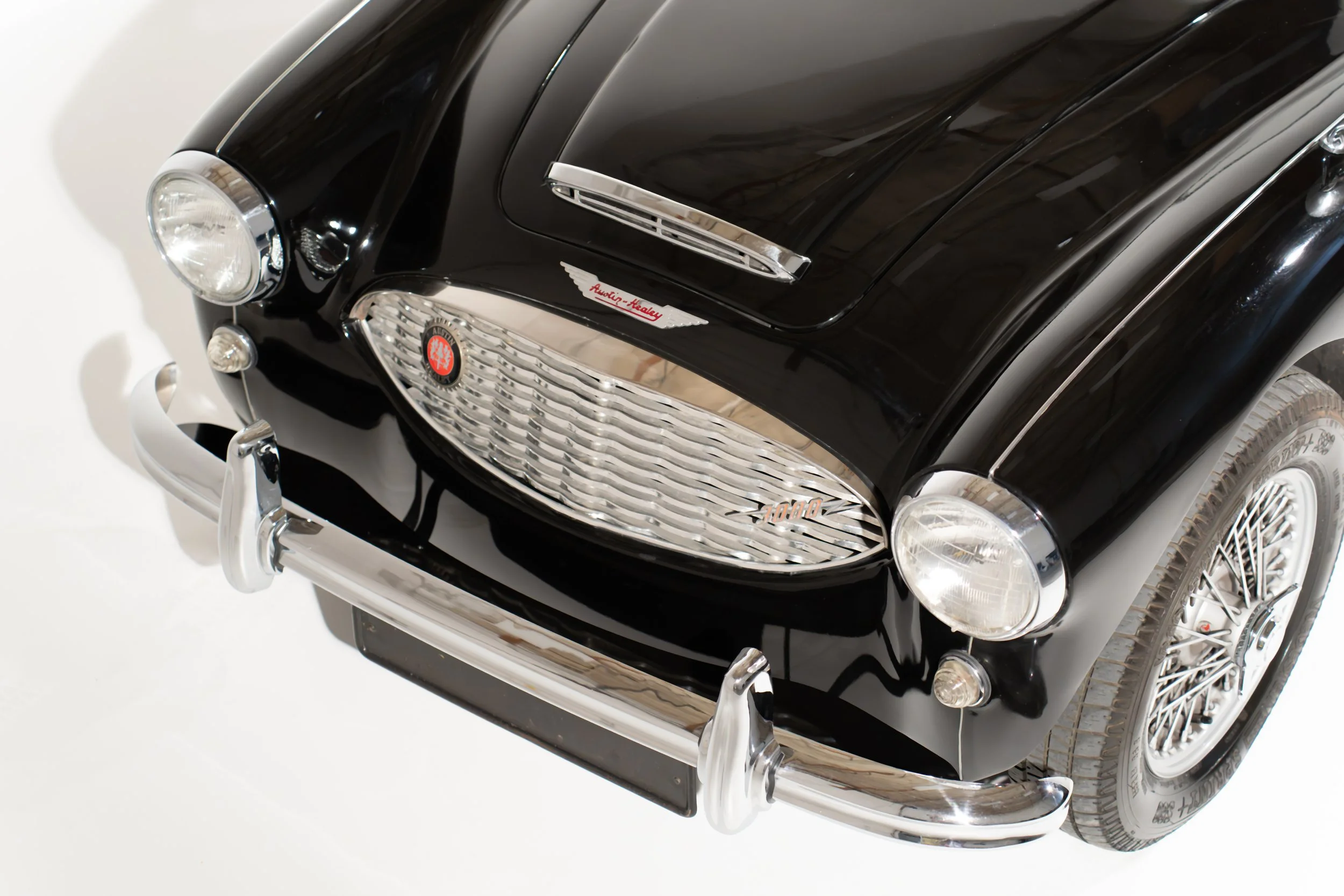 A black vintage style toy car with shiny silver accents, a front grille, headlights, and a badge on the hood that says 'Audi-Keady,' viewed from a front-side angle.