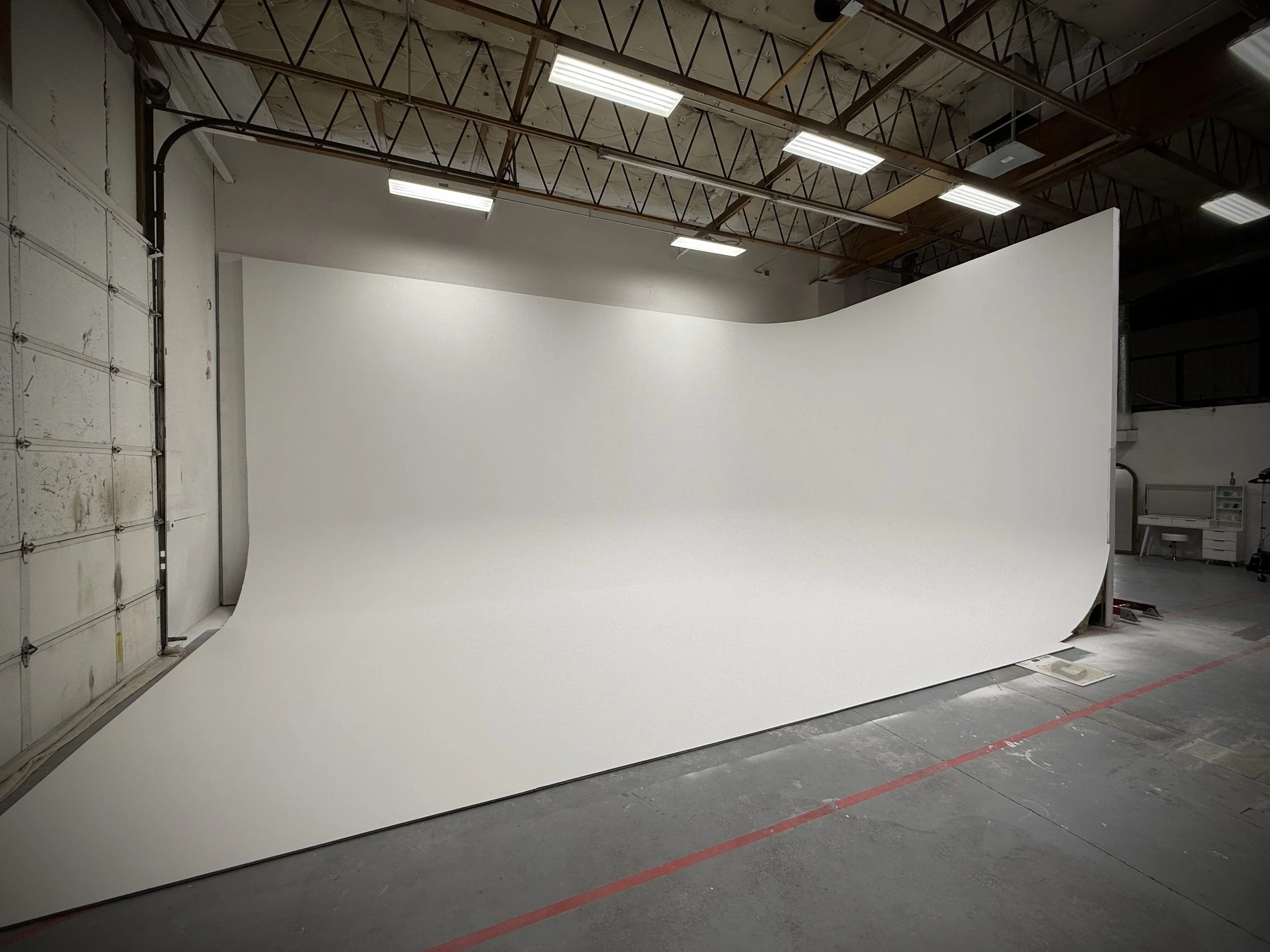 A large white curved photography backdrop in a studio, with industrial ceiling and fluorescent lights overhead.