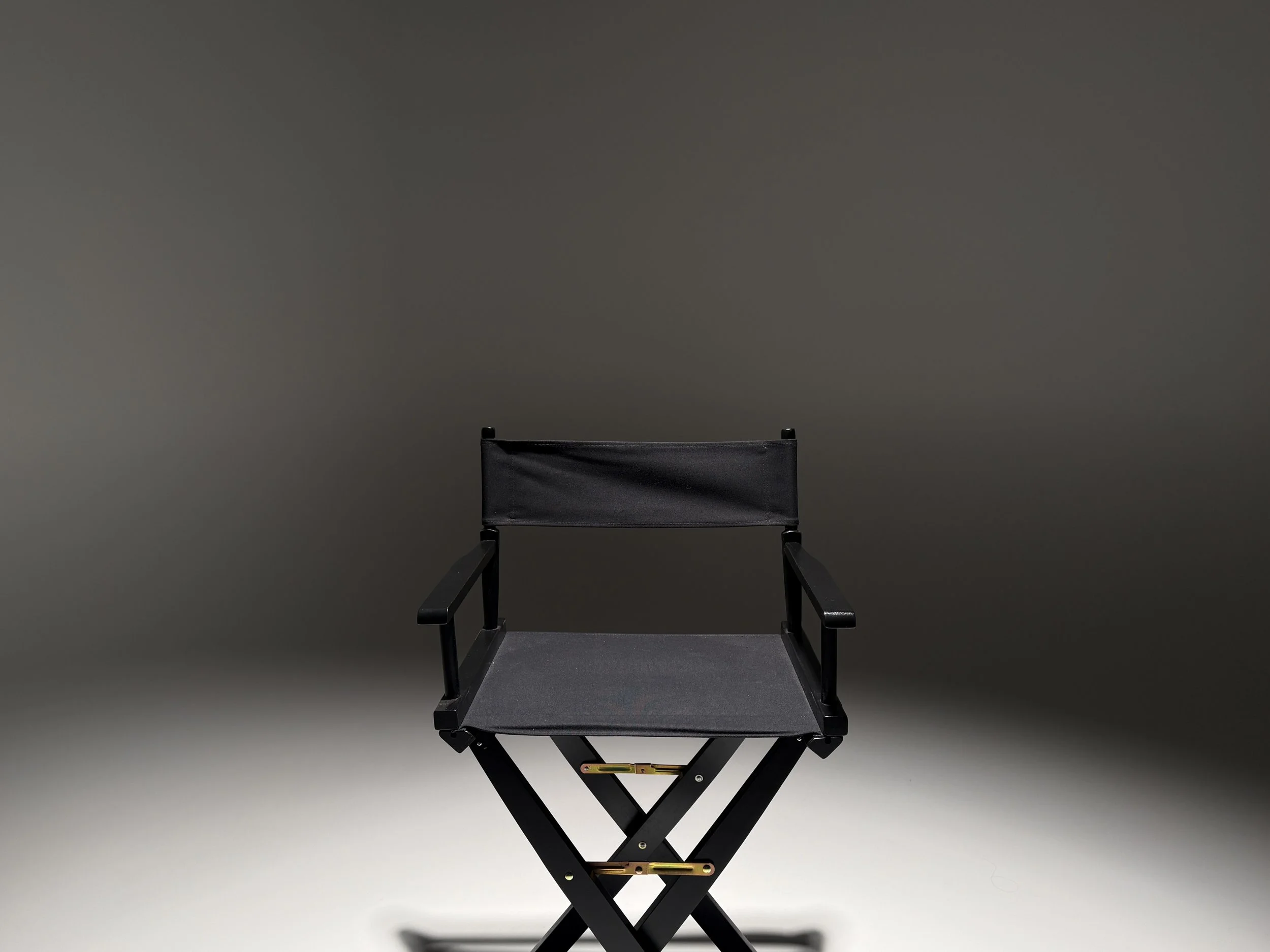A black director's chair with a folding black frame and a slightly textured black fabric seat and backrest, set against a plain gray background.