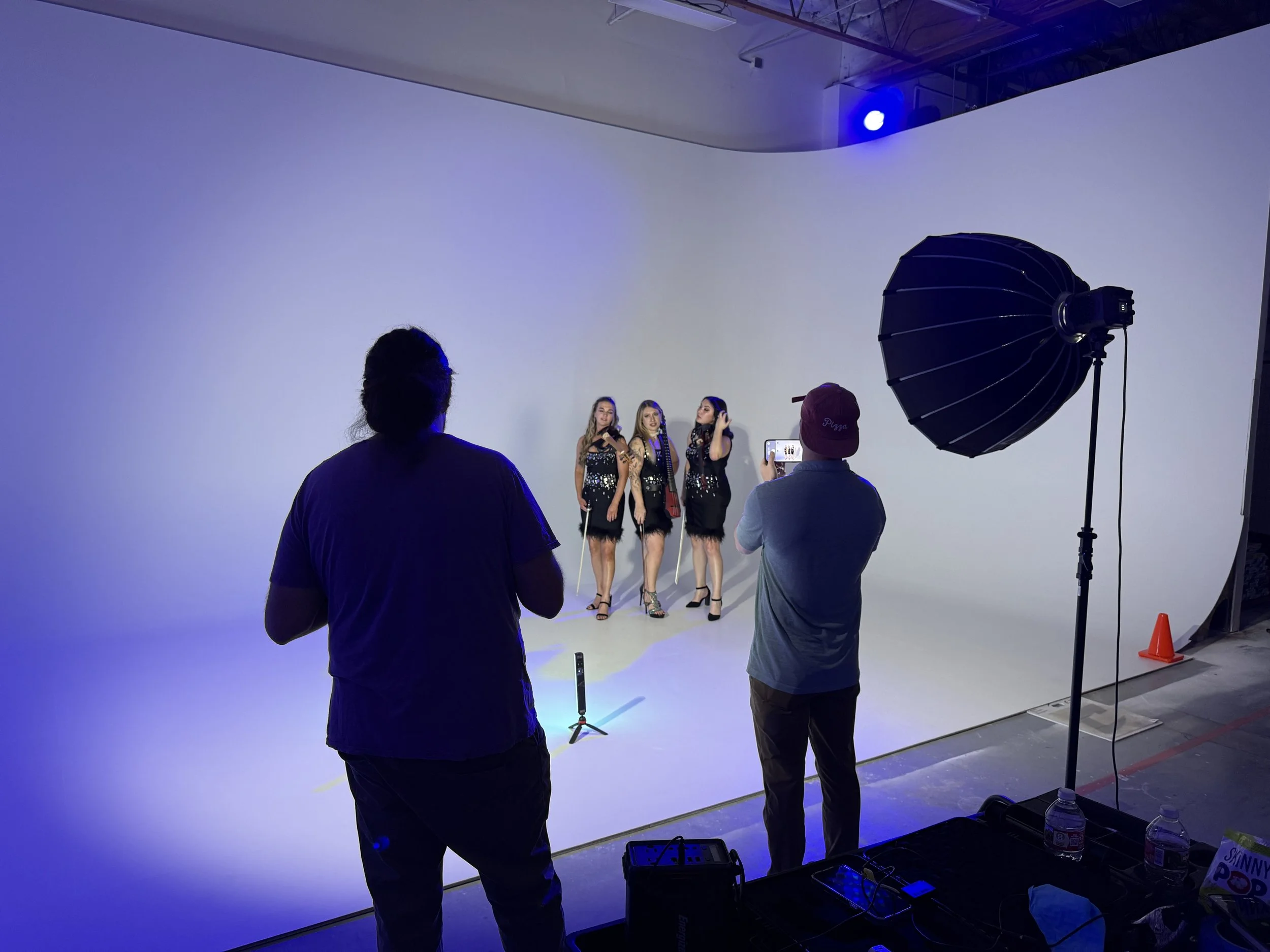 People participating in a photo shoot in a professional studio with a large white backdrop, studio lighting, and equipment.