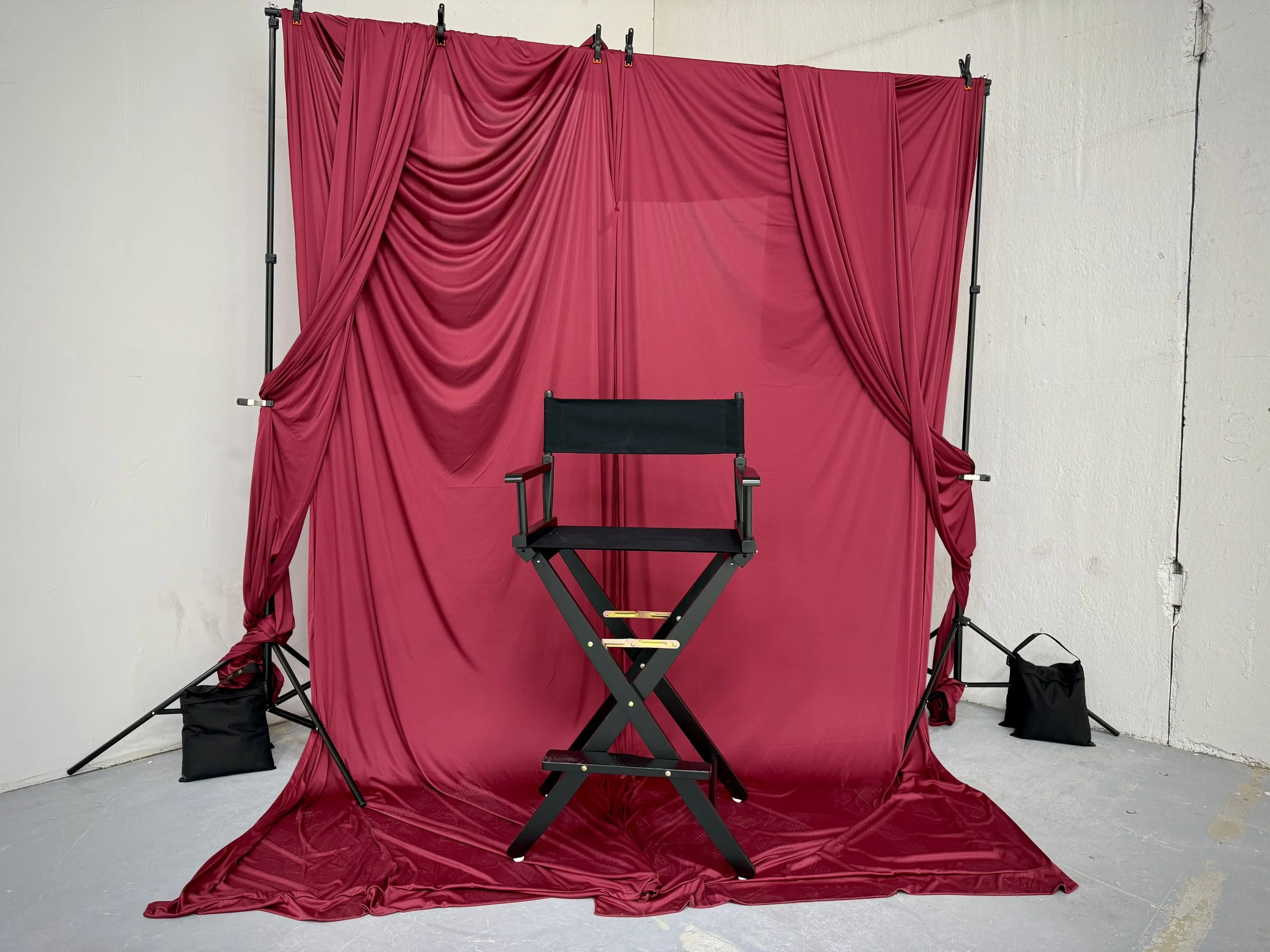 Red theater stage curtain backdrop with a director's chair in front, set up for a performance or photoshoot.