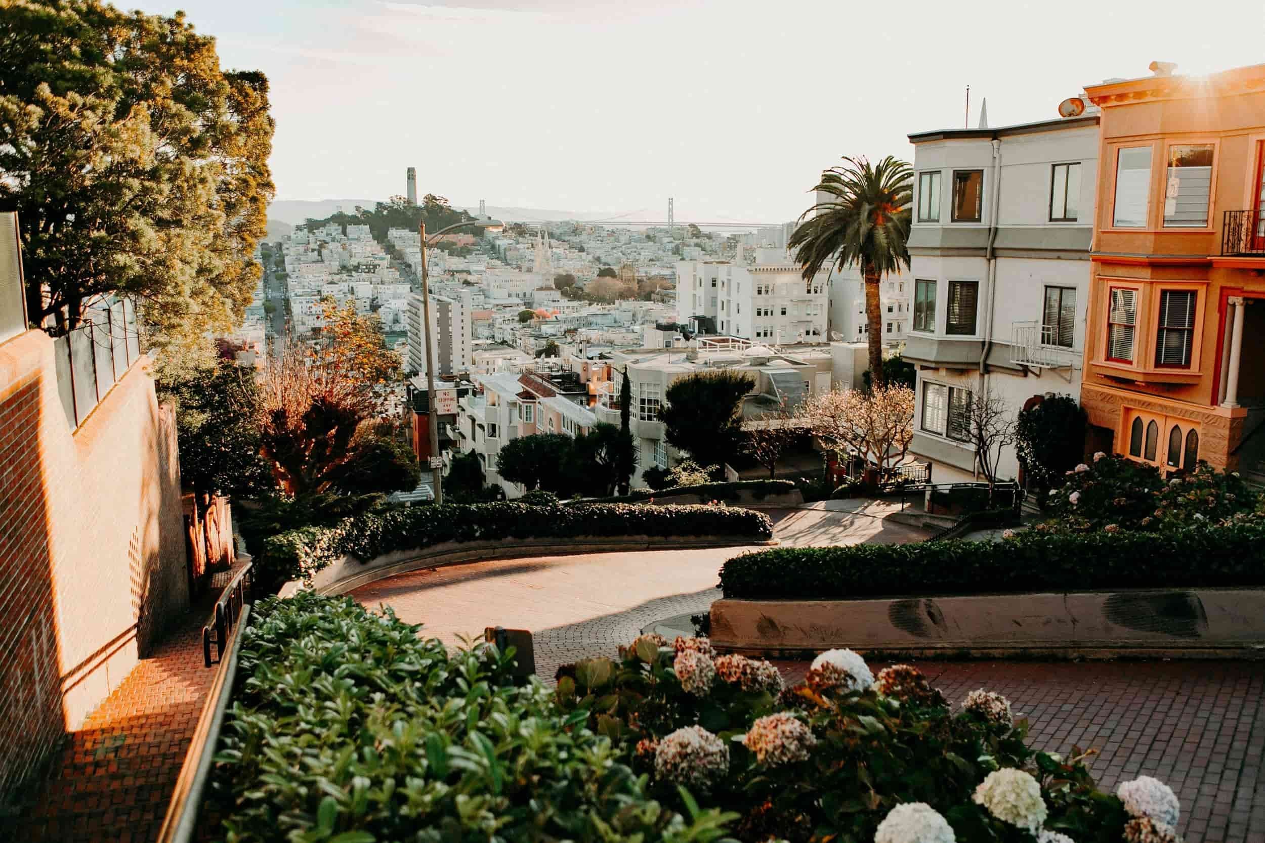 View of Lombard Street in San Francisco, featuring winding brick road, greenery, and cityscape in the background, with a clear sky.