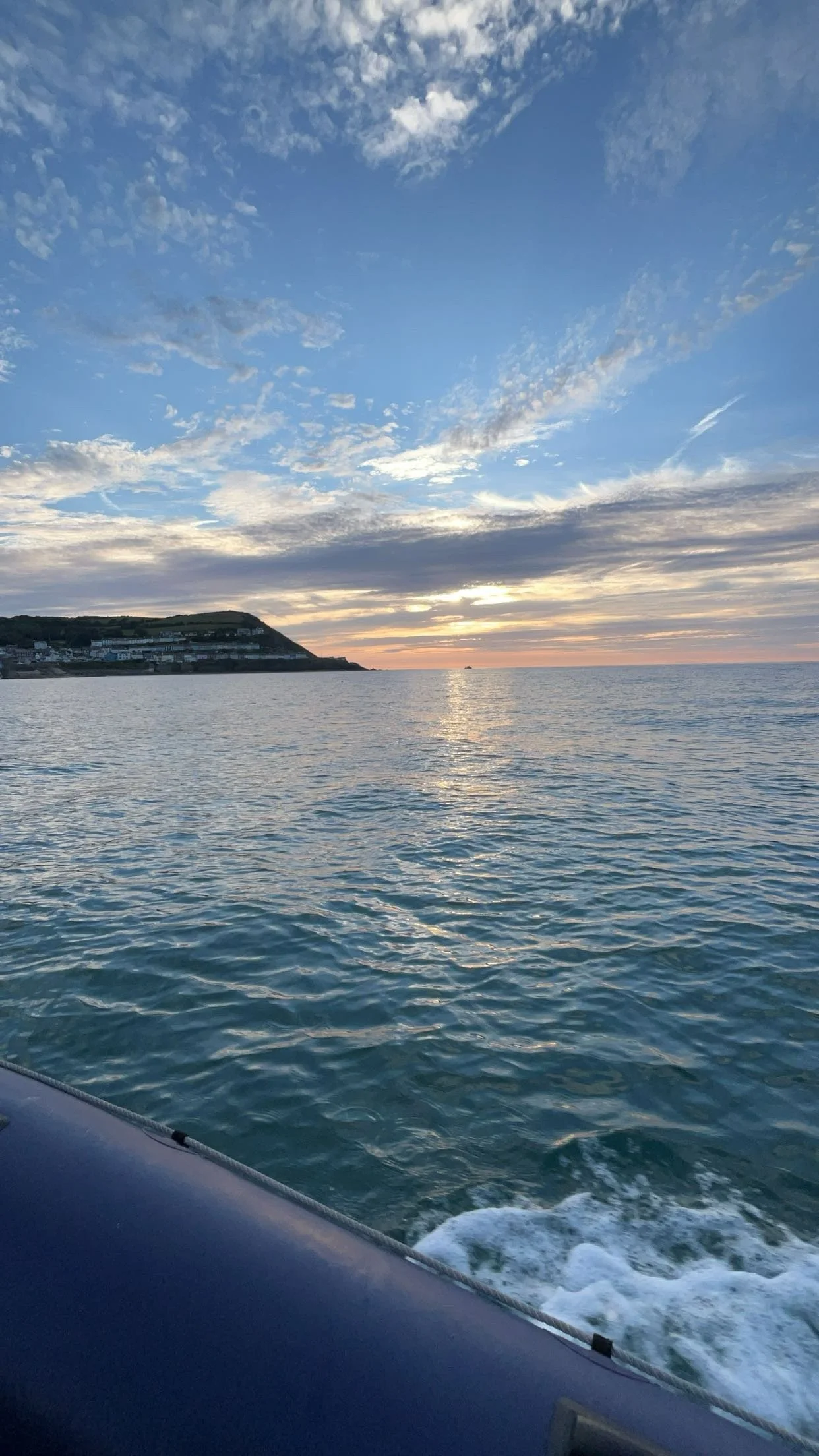 Ocean view at sunset with clouds and distant hills.
