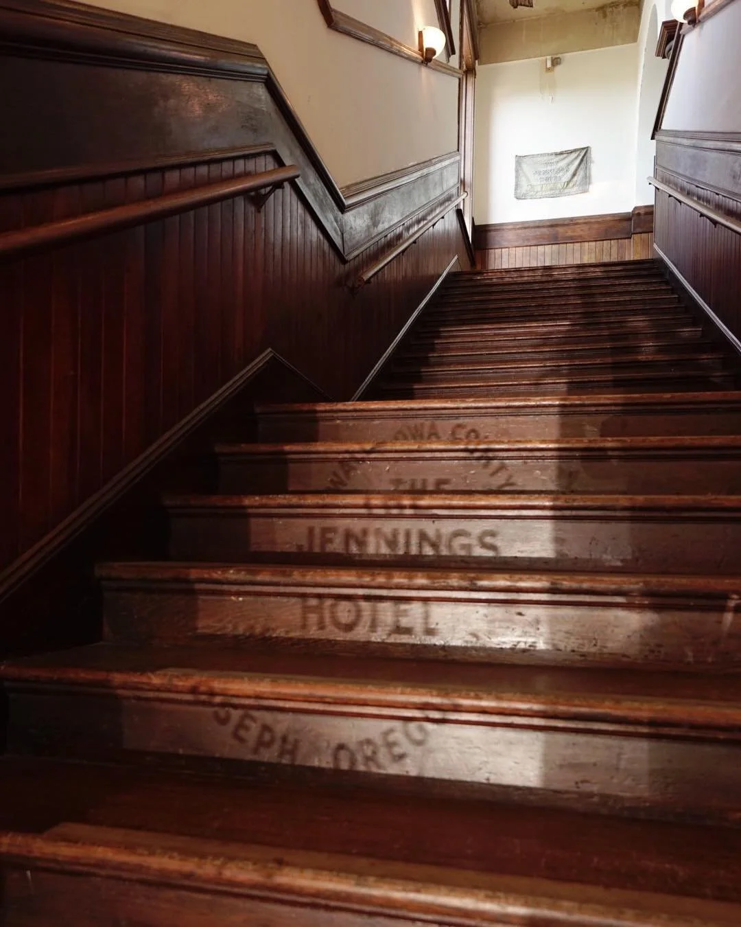 Wooden staircase with faded text on the steps, leading to an upper floor in a historic building.