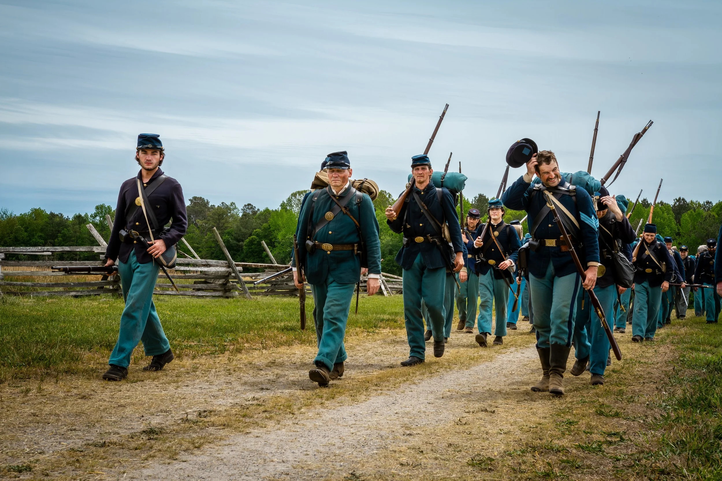 People dressed as Civil War soldiers walking outdoors in a field under cloudy sky.