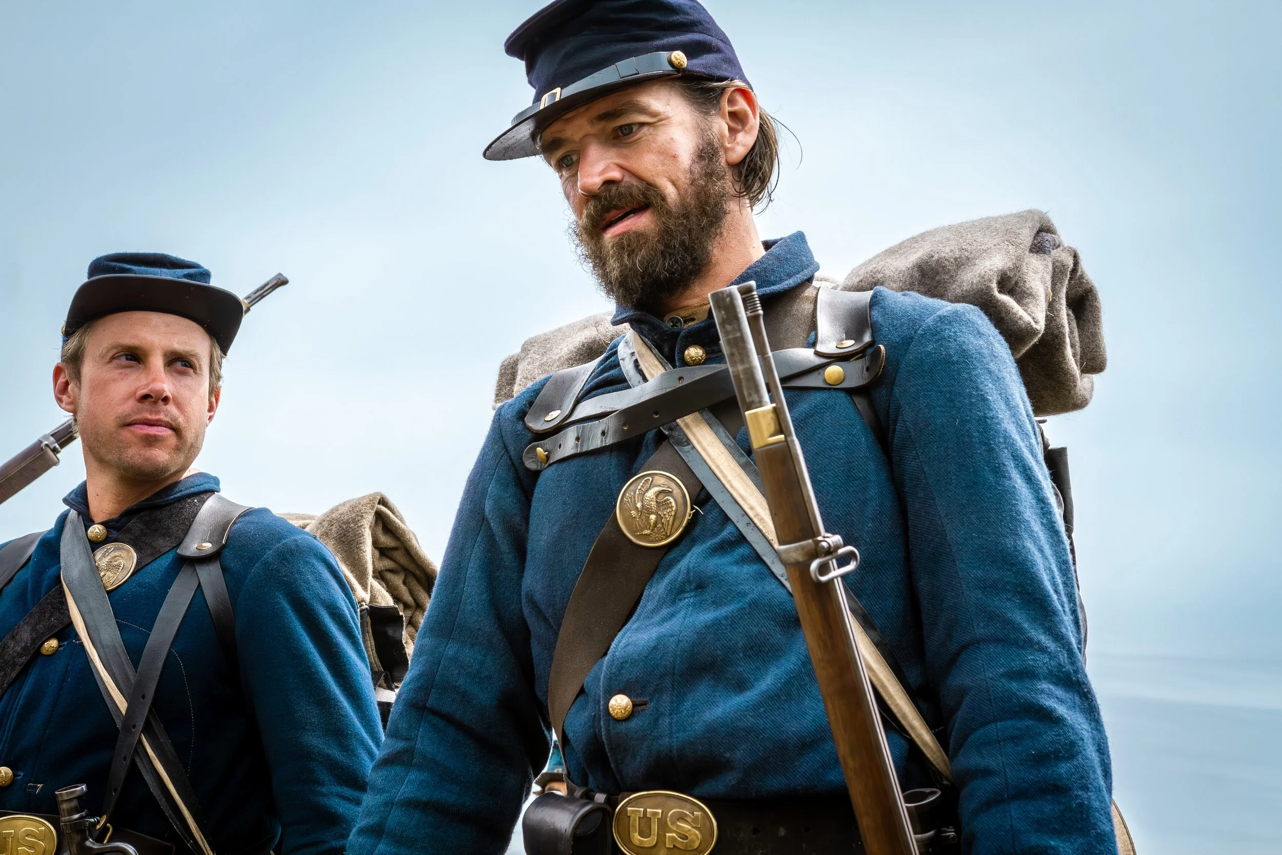 Historical reenactors dressed as Union soldiers from the American Civil War, wearing blue uniforms with gold buttons and badges, carrying rifles and backpacks.