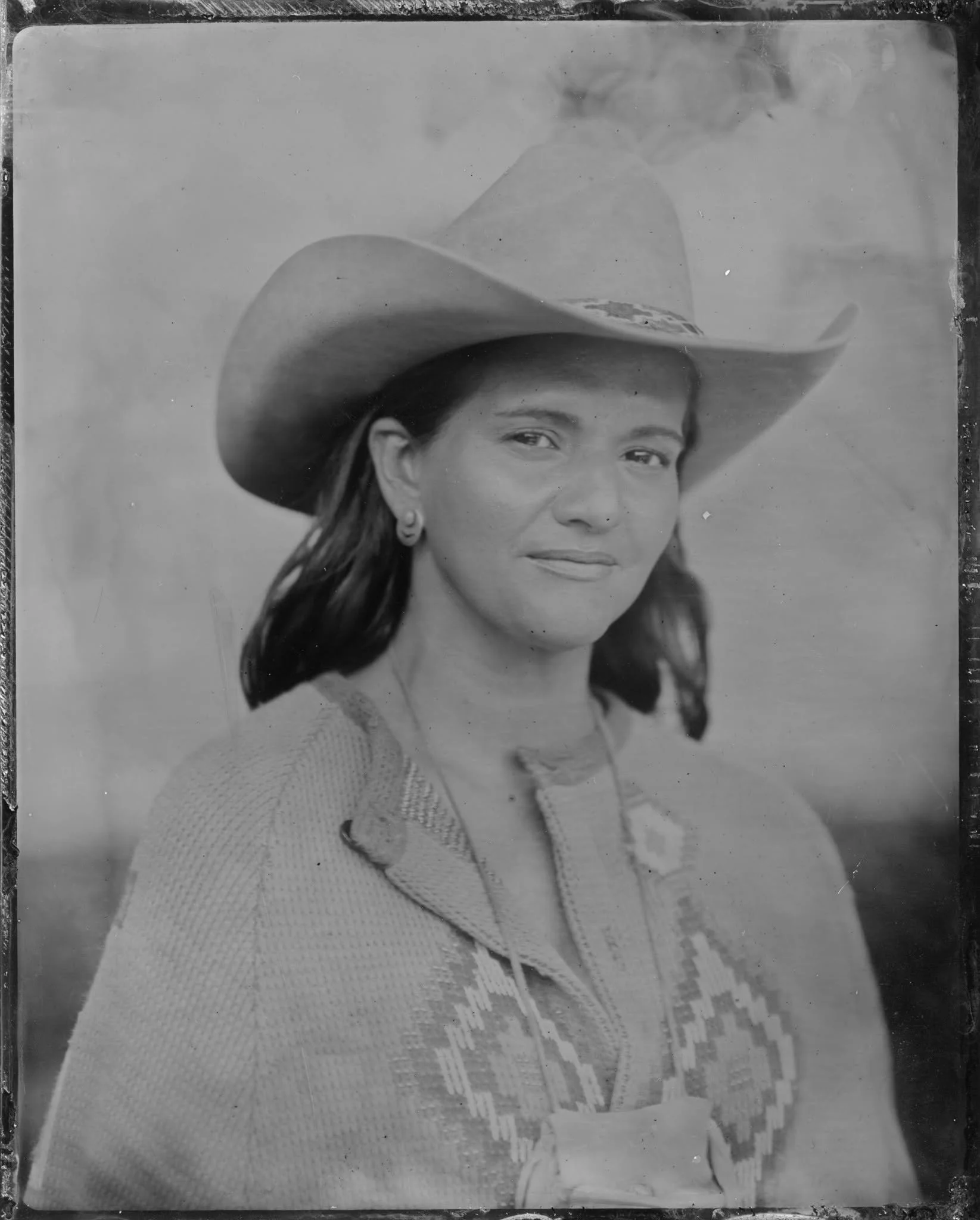 Black and white photo of a woman wearing a large hat, a necklace, earrings, and a sweater, with her face turned to the side.