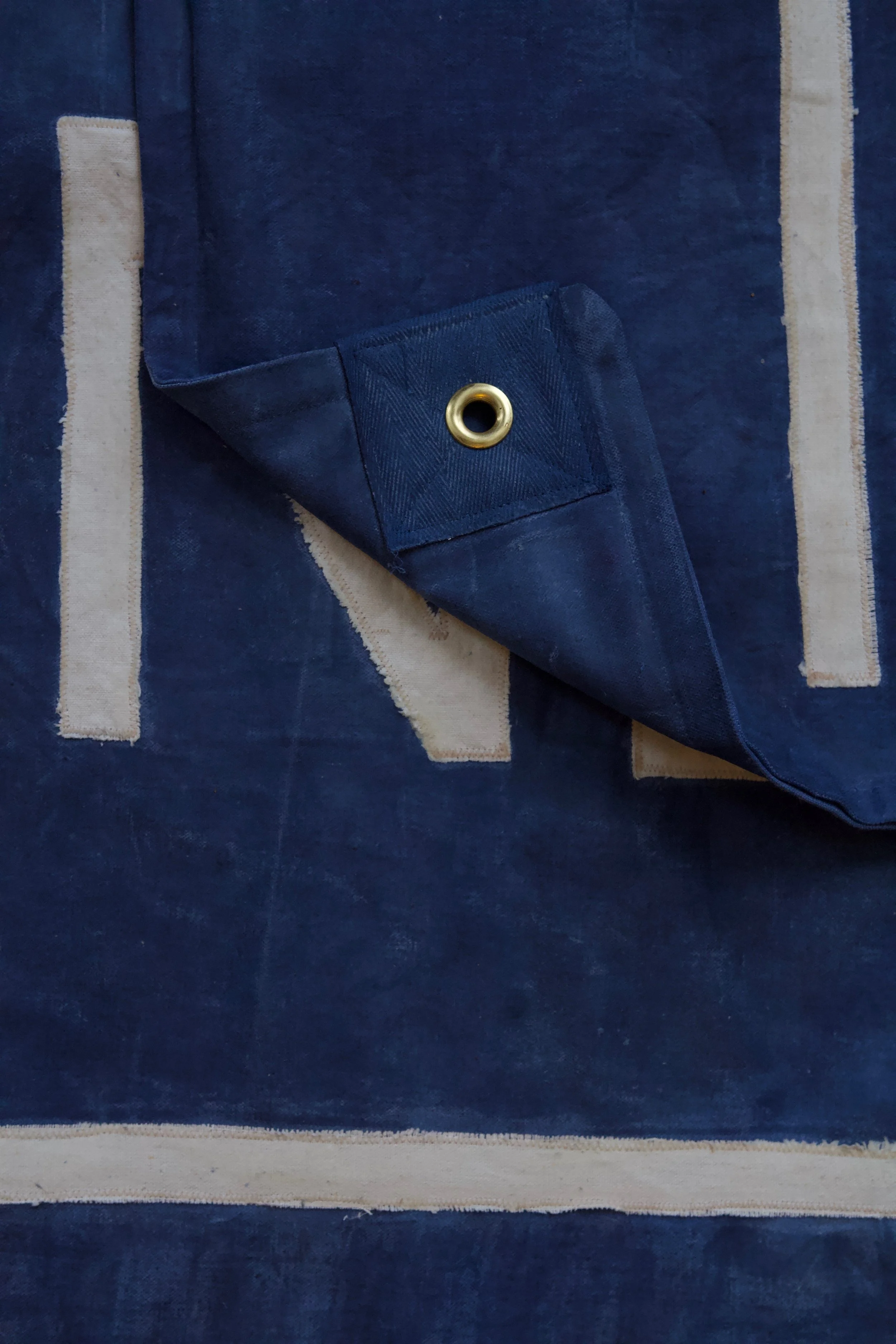 Close-up of a navy blue fabric with a brass grommet, folded corner, resting on a blue and white striped hemp fabric flag.