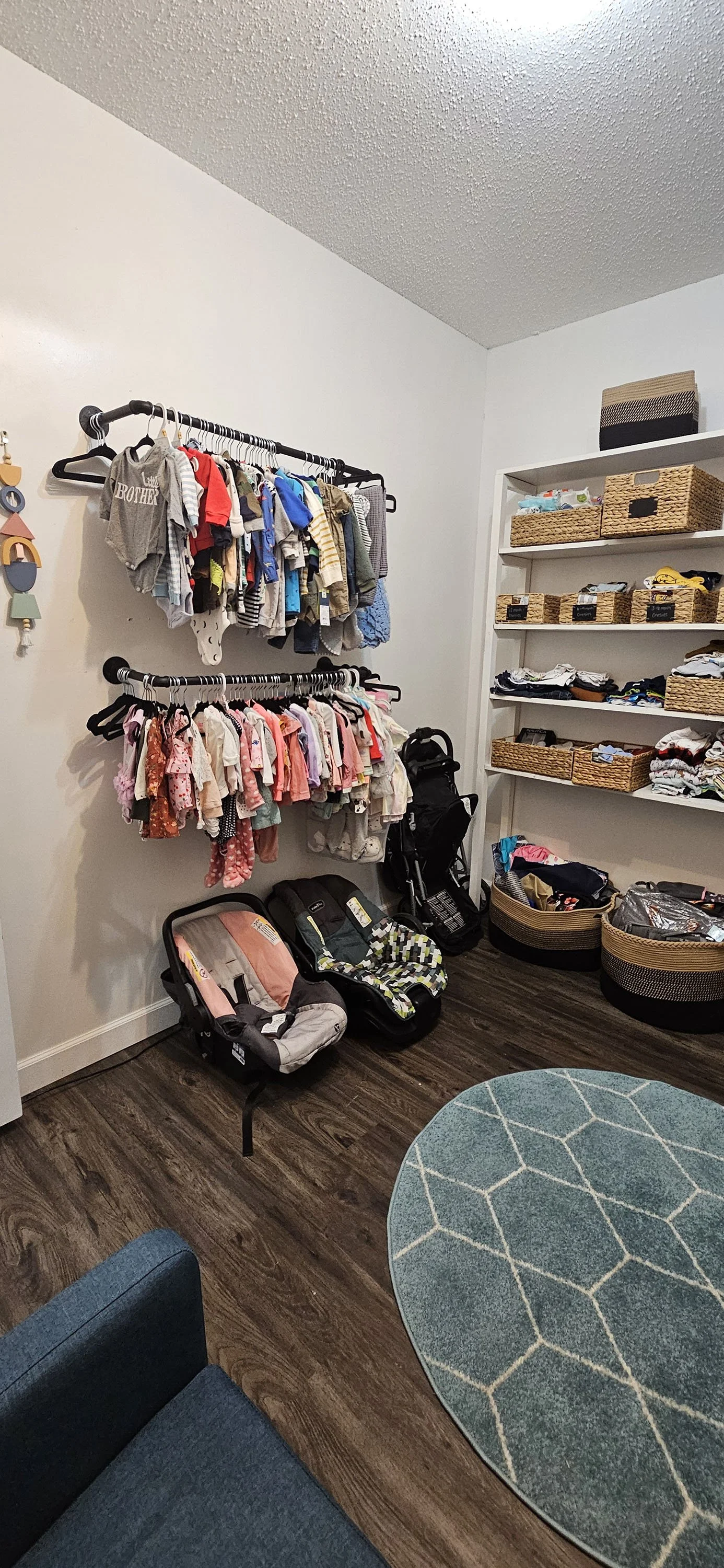 Baby nursery closet with hanging clothes, car seats, and shelves with baskets.