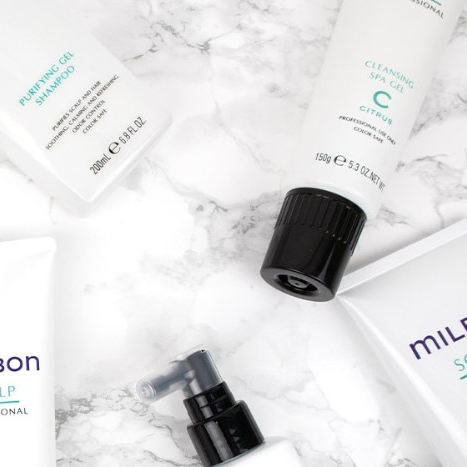 Arrangement of skincare products on marble surface, including cleansing gel, purifying foam shampoo, calming serum, and a spray bottle.