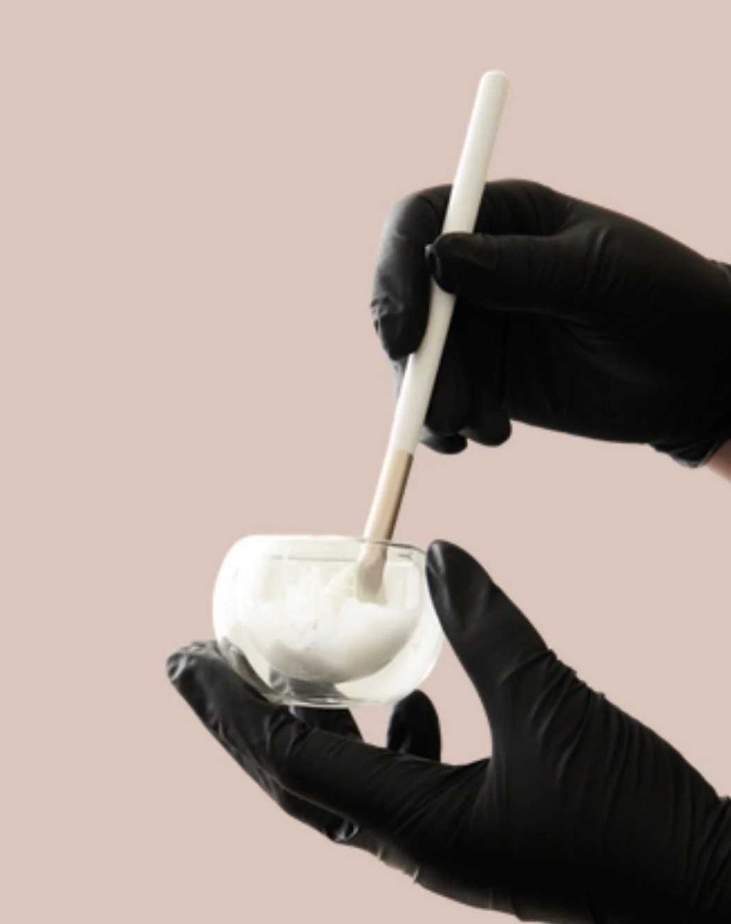 Person wearing black gloves holding a small glass bowl and a moxie stick, preparing to dip the stick into the bowl.