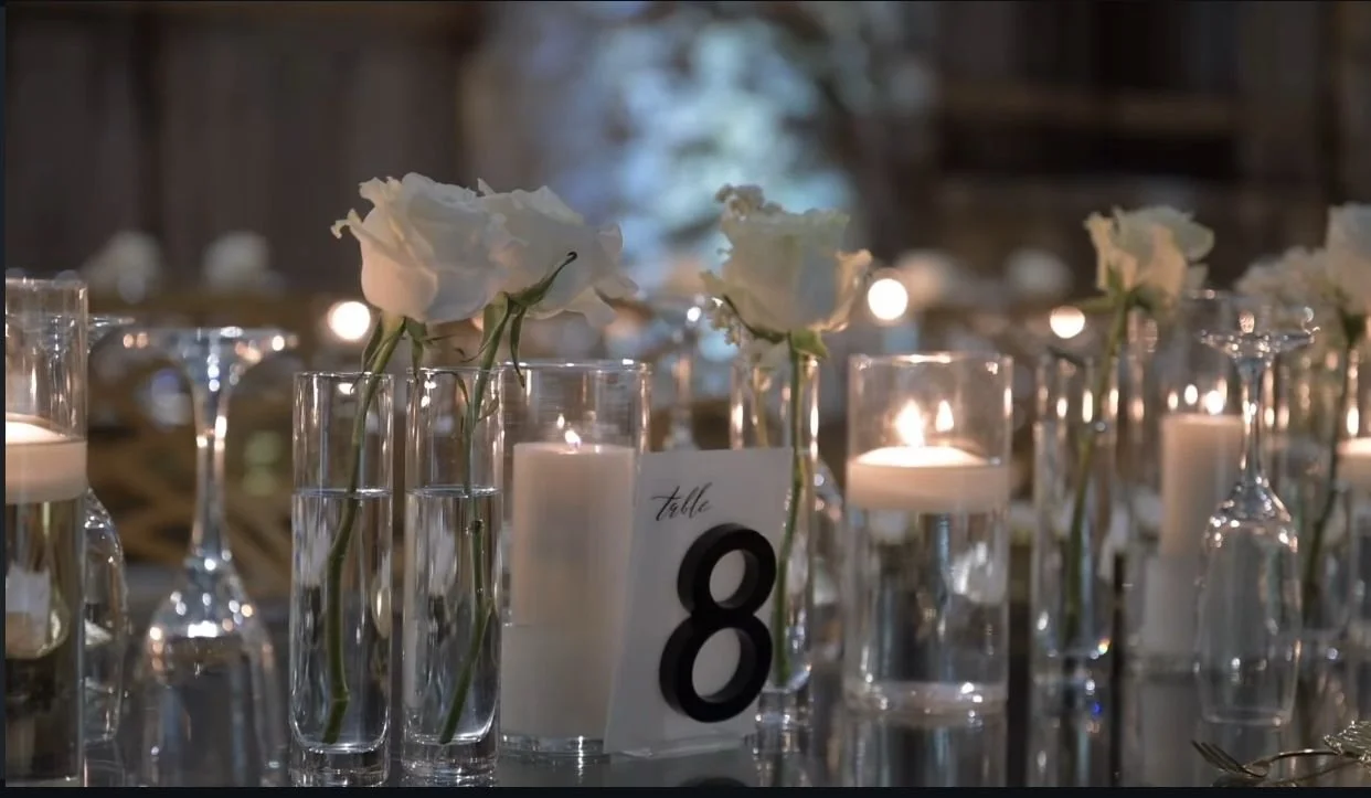 Table setting with white flowers in glass vases, candles in glass holders, and a table number card labeled 8.