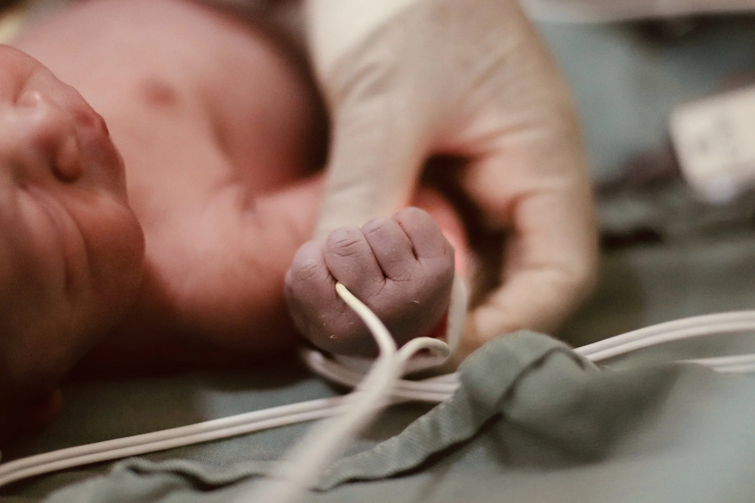 Close-up of a newborn baby's face and hand, showing the baby's eye, nose, lips, and tiny fist, with a hand softly supporting the baby's head.