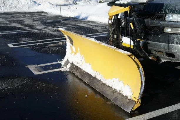 A snow plow attached to a black truck clearing snow from parking lot.