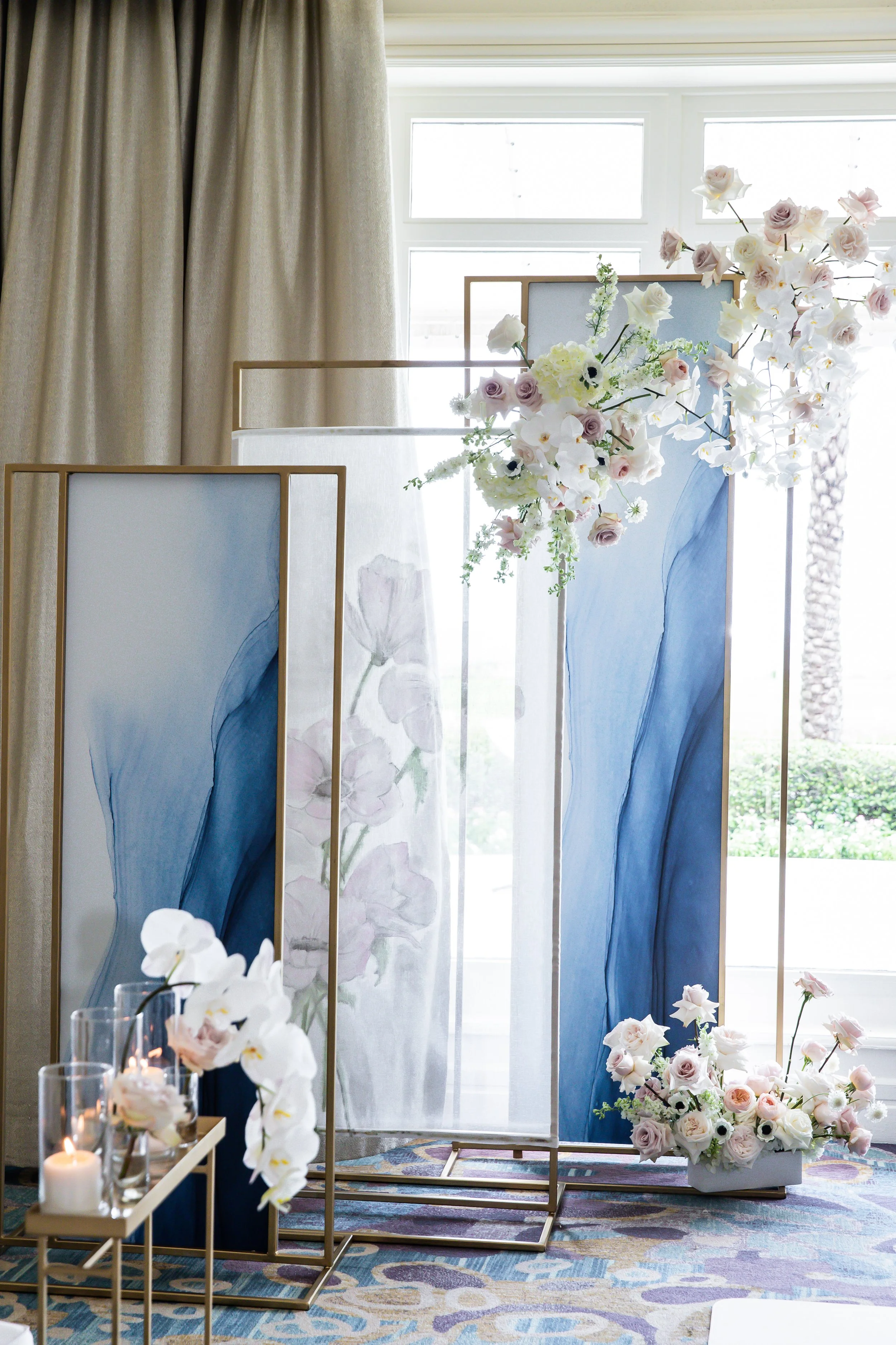 Decorative wedding backdrop with floral arrangements, blue and white color scheme, and candles.