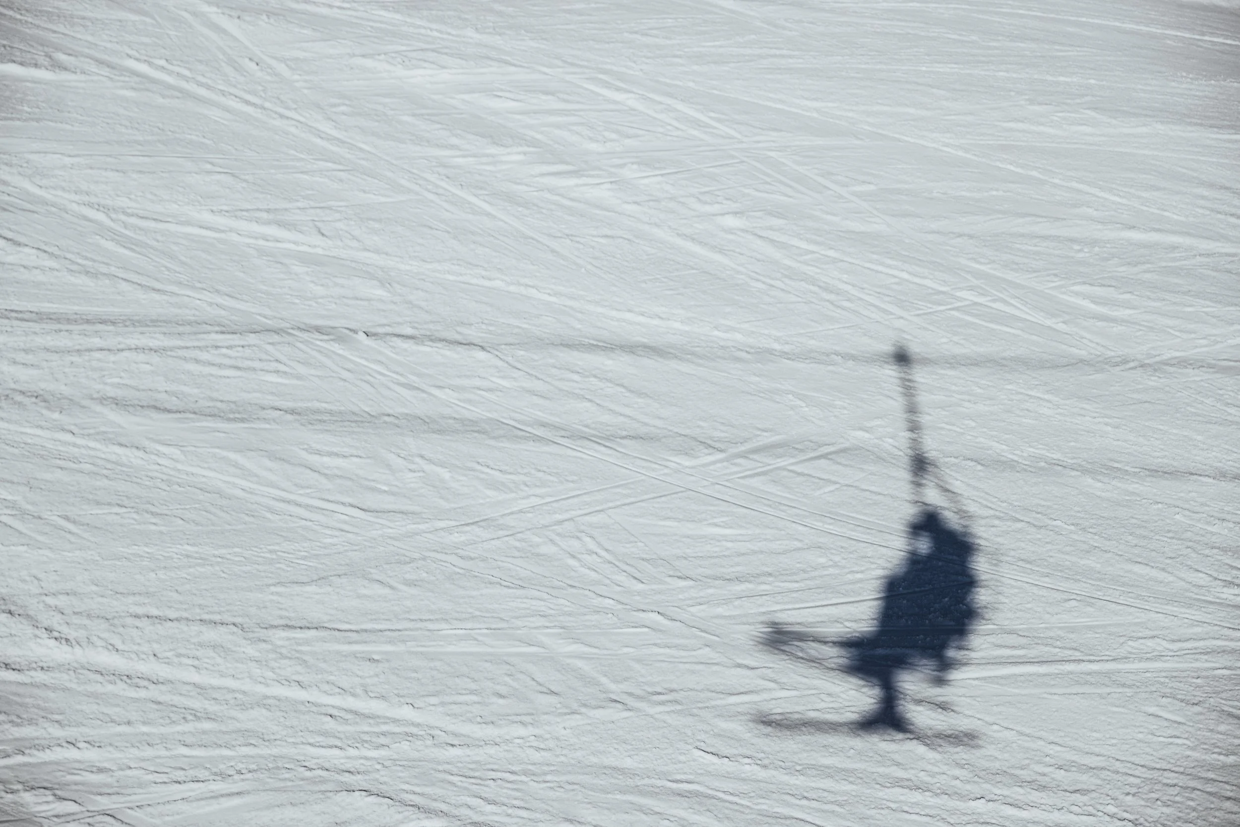 Shadow of a person skiing on snowy terrain with ski poles and skis, with ski tracks in the snow.