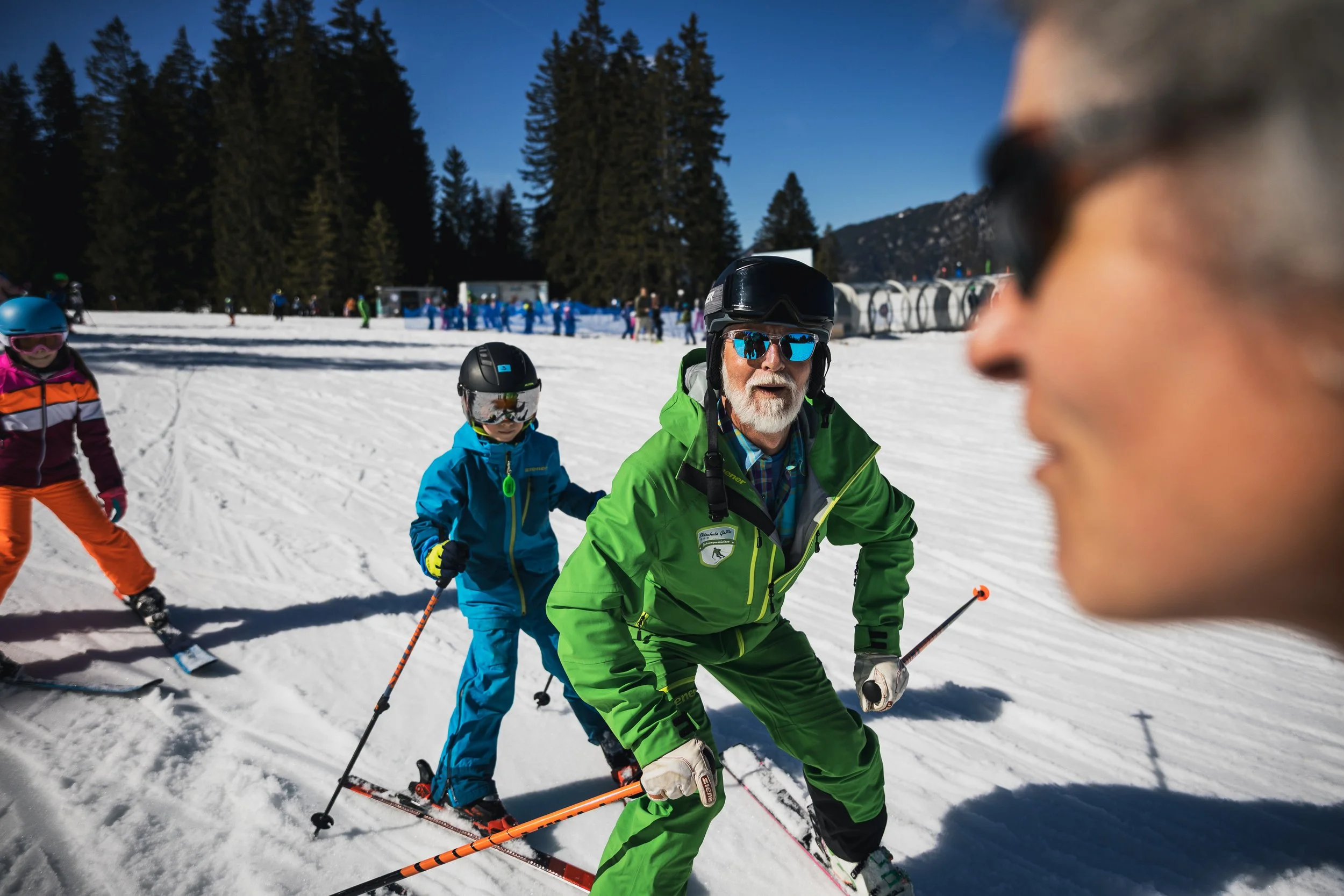People skiing on a snowy mountain with trees and mountains in the background.