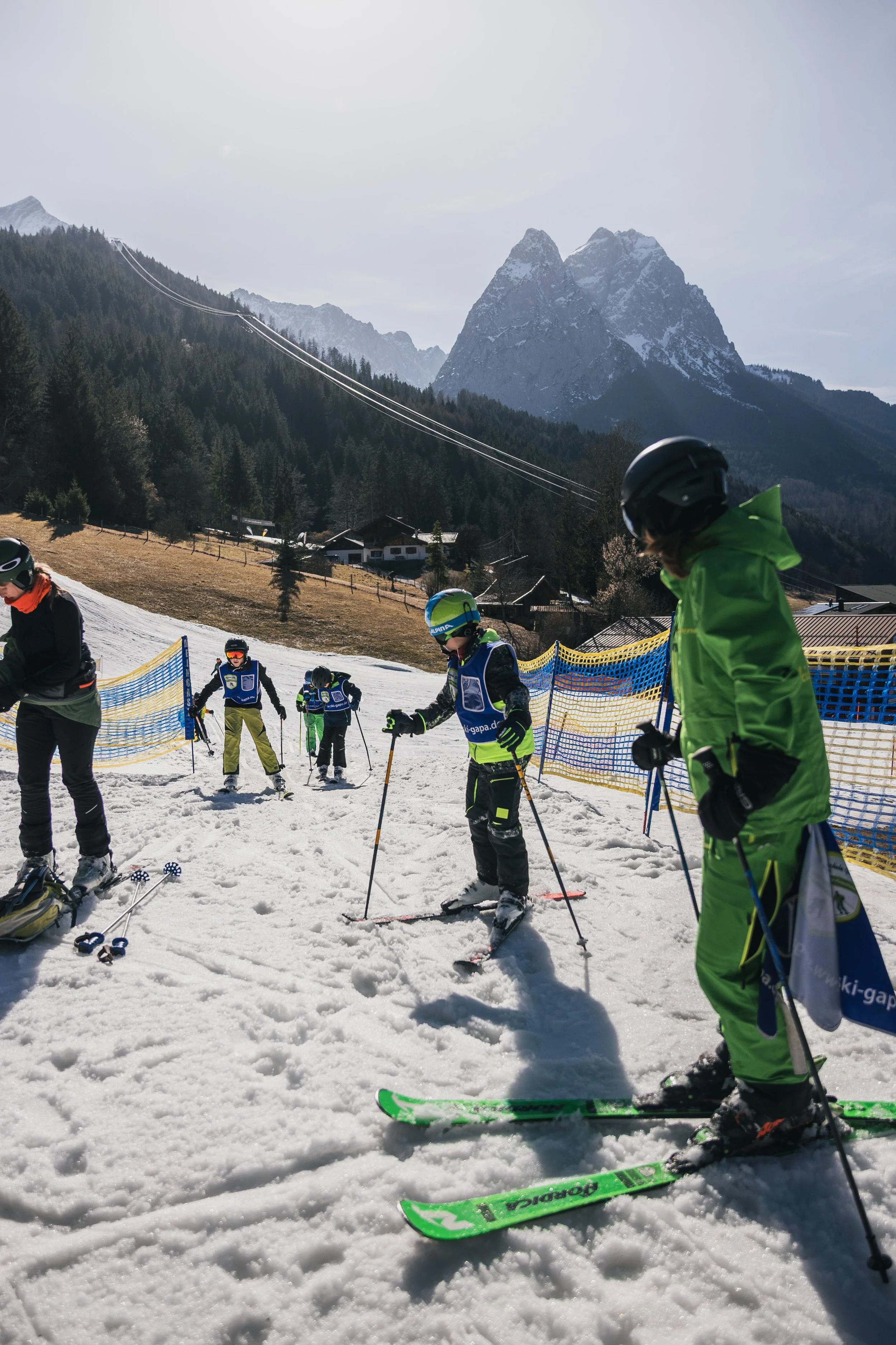 Group of children skiing on a snowy mountain slope with mountains in the background.