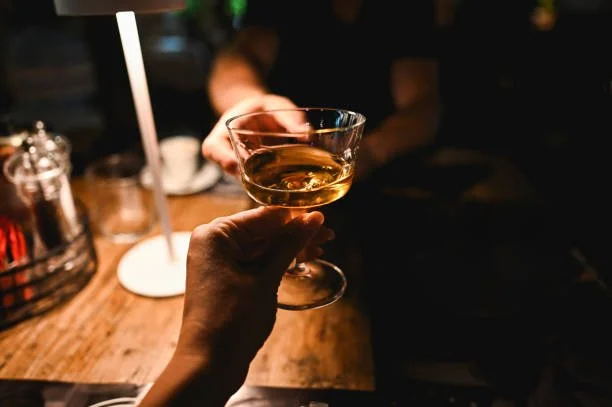 Close-up of a hand holding a cocktail glass filled with a brown liquid at a bar or nightclub.