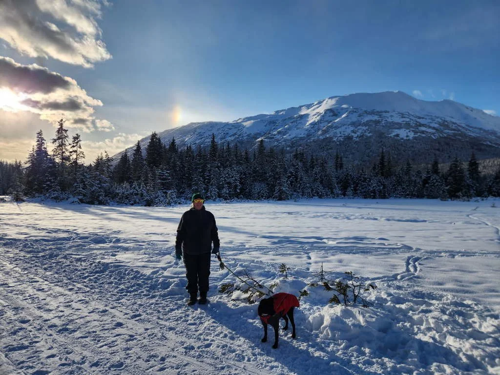 Woman outside in the winter holding dog on a leash with mountains in the background