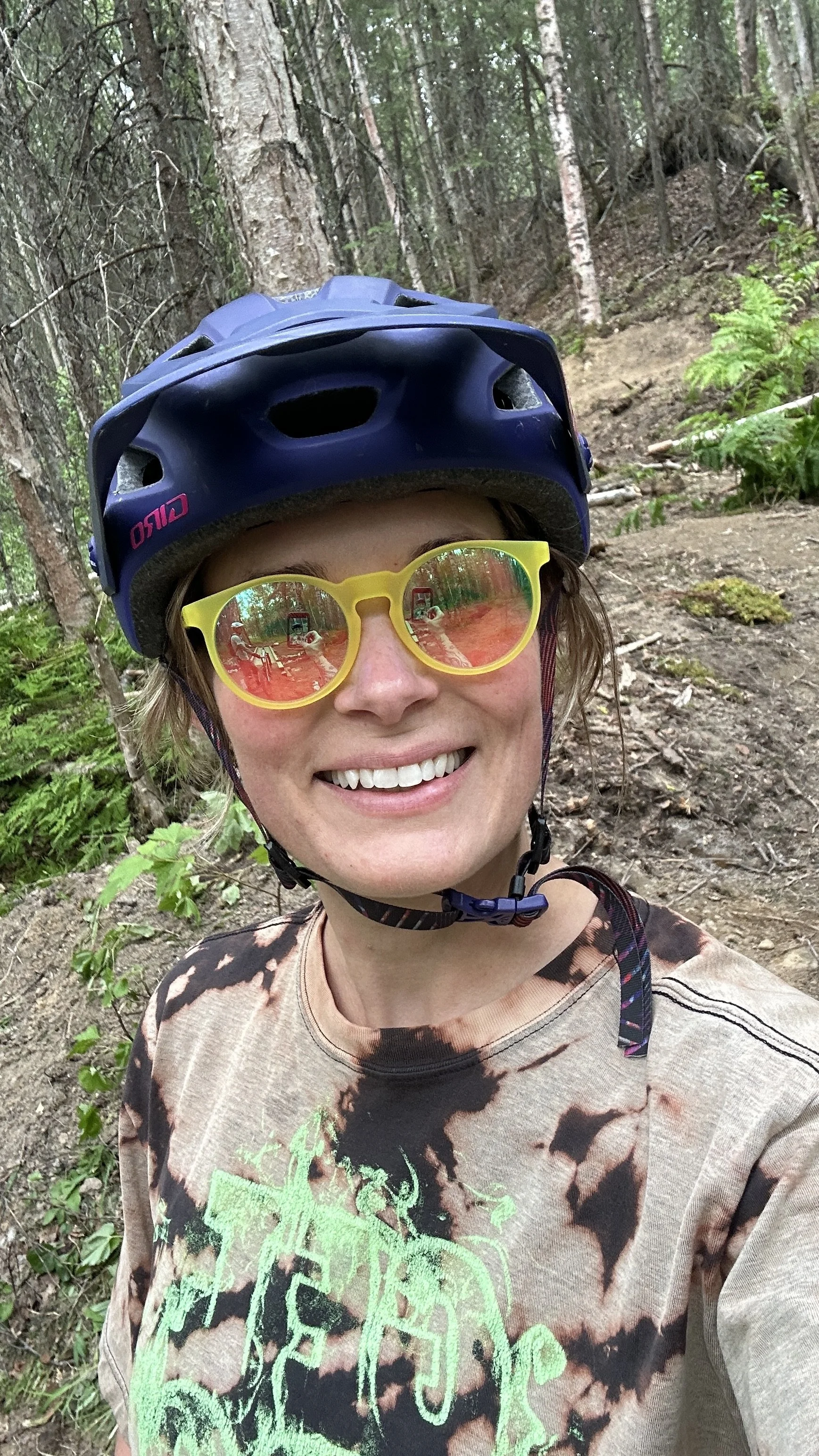 Woman smiling with yellow sunglasses on wearing a bike helmet outside on a trail