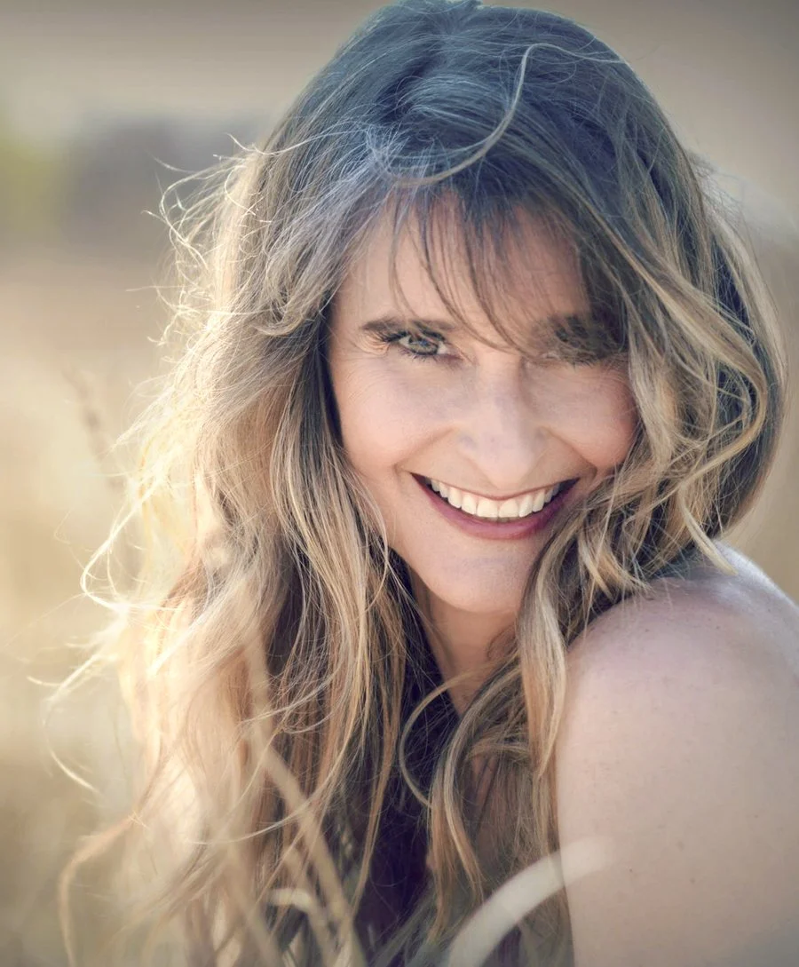 Woman with long blonde hair smiling outside in the summer under sunshine